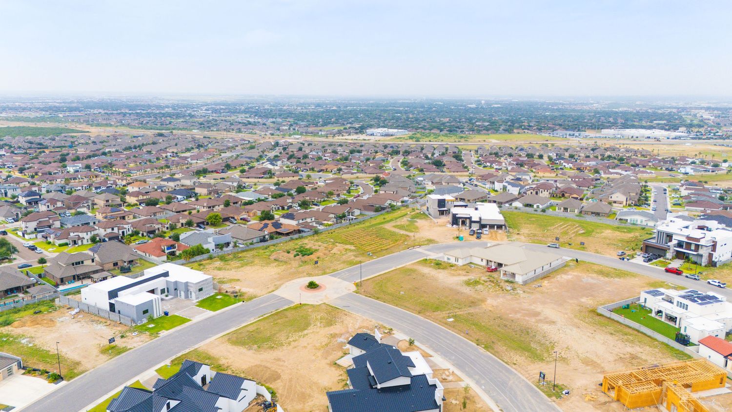 Aerial panoramic view of a residential development with scattered homes and buildings across dry terrain.