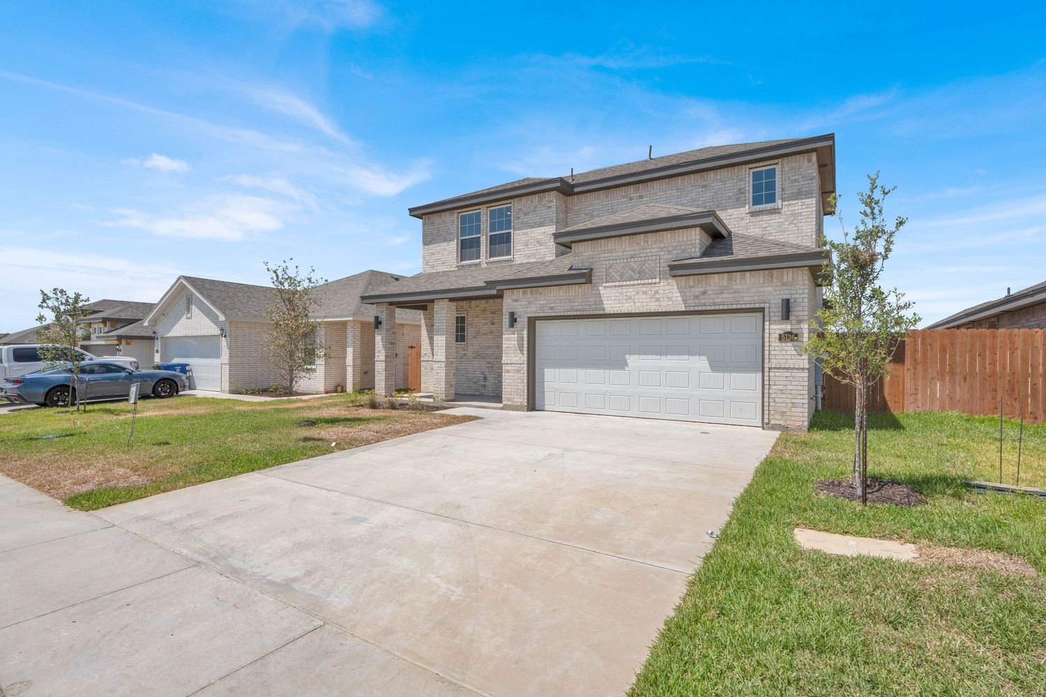 Two-story brick and stucco home with three-car garage, concrete driveway, and manicured lawn under blue skies.