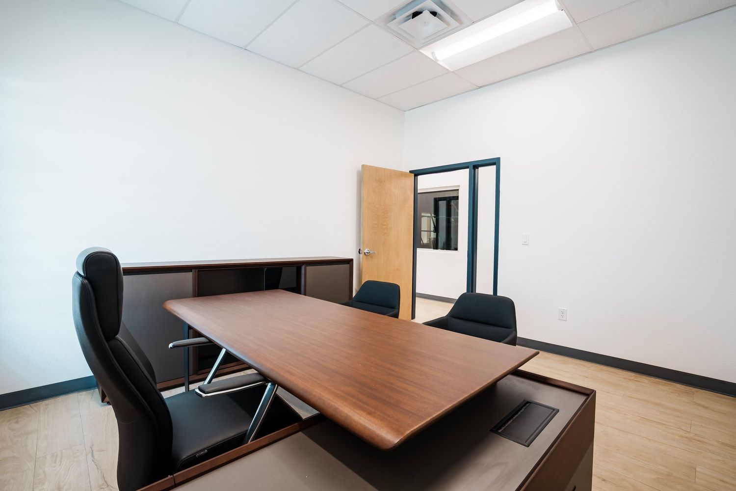 Empty conference room with wooden table, black office chairs, and fluorescent lighting in a modern office setting.