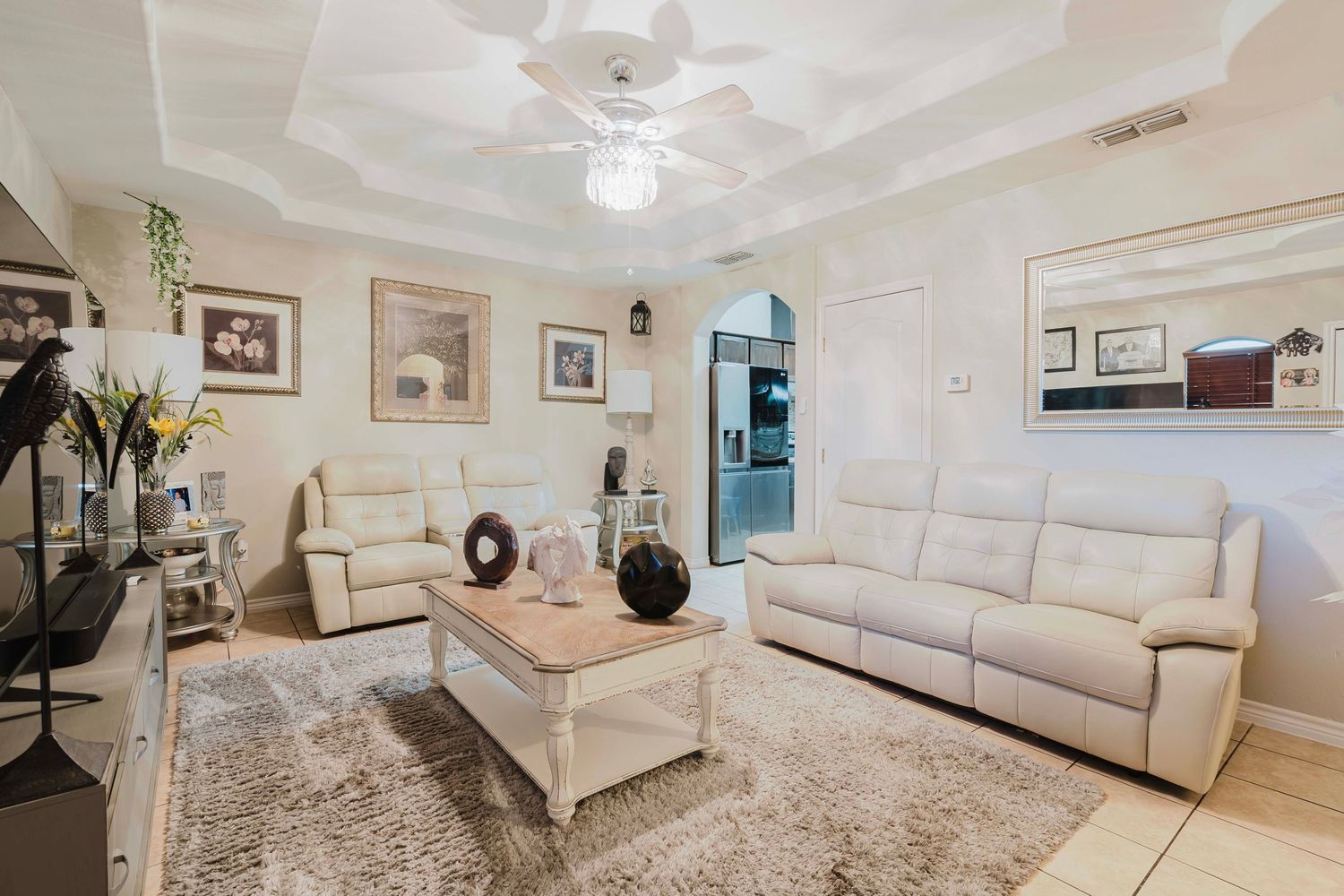 Modern living room with cream sectional sofa, plush area rug, stylish coffee table and ceiling fan in white interior.
