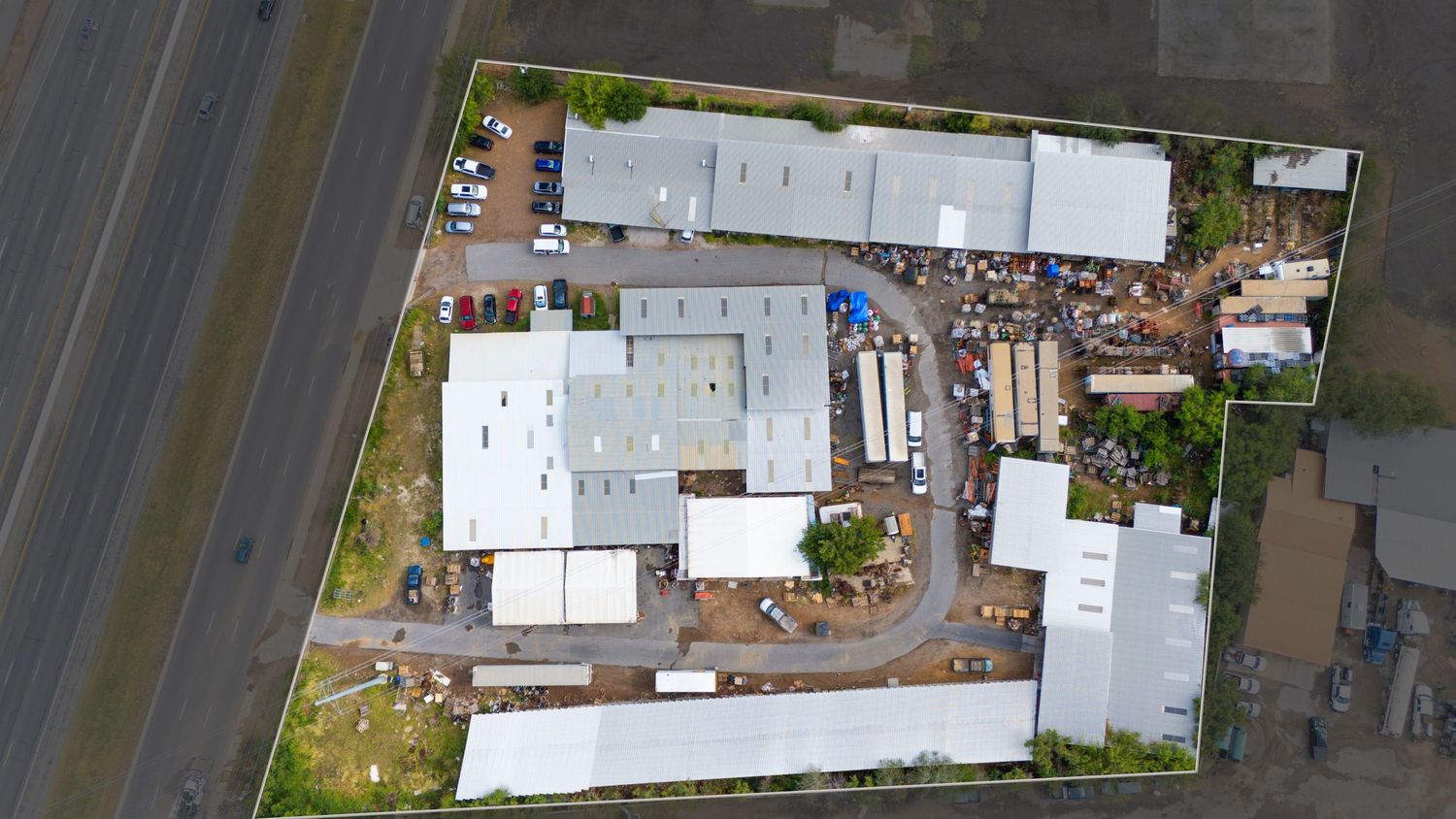 Aerial view of industrial complex with white buildings, storage yards, and curved driveway layout on commercial property.