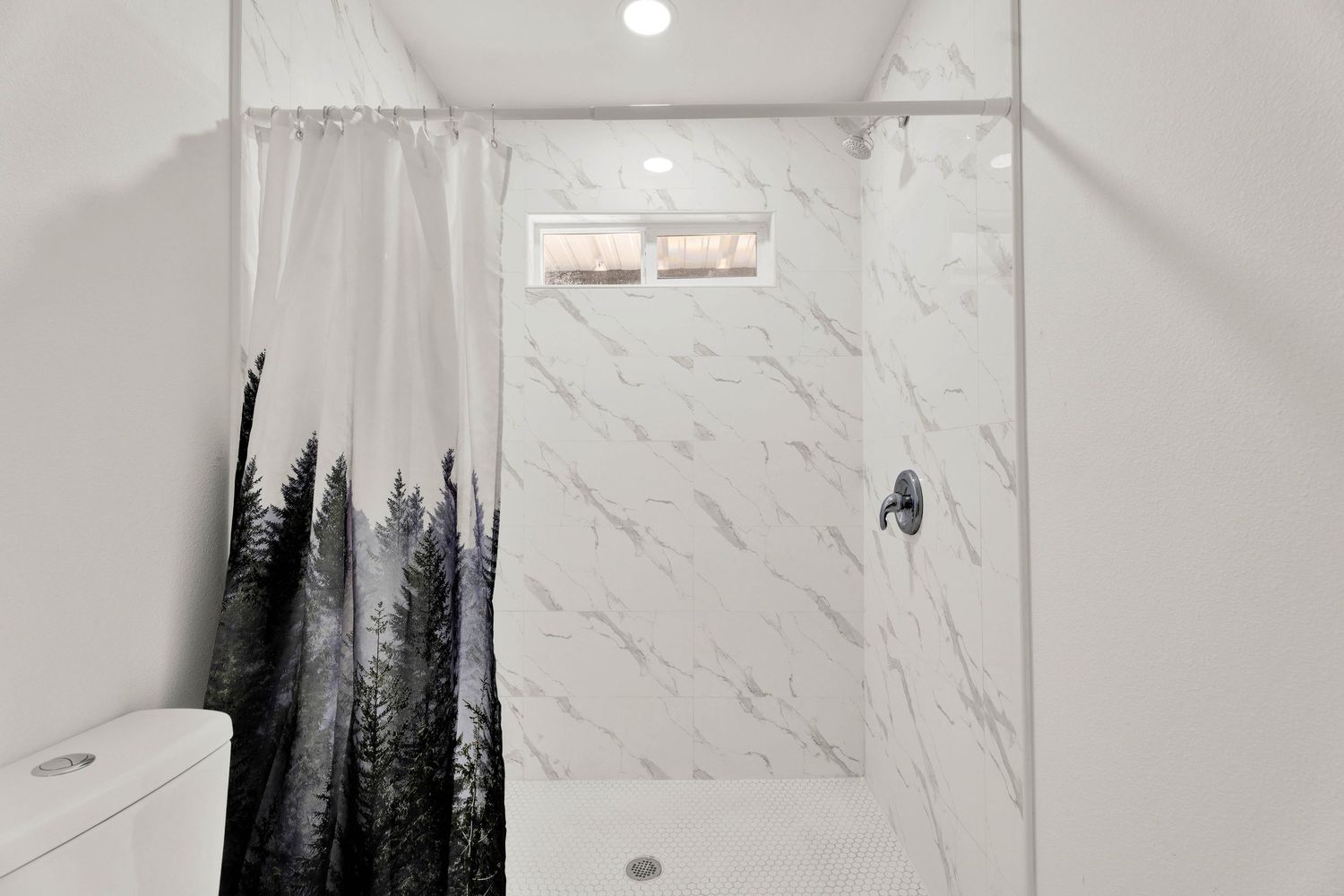 Elegant marble tile shower with forest print curtain, window, and chrome shower fixture.