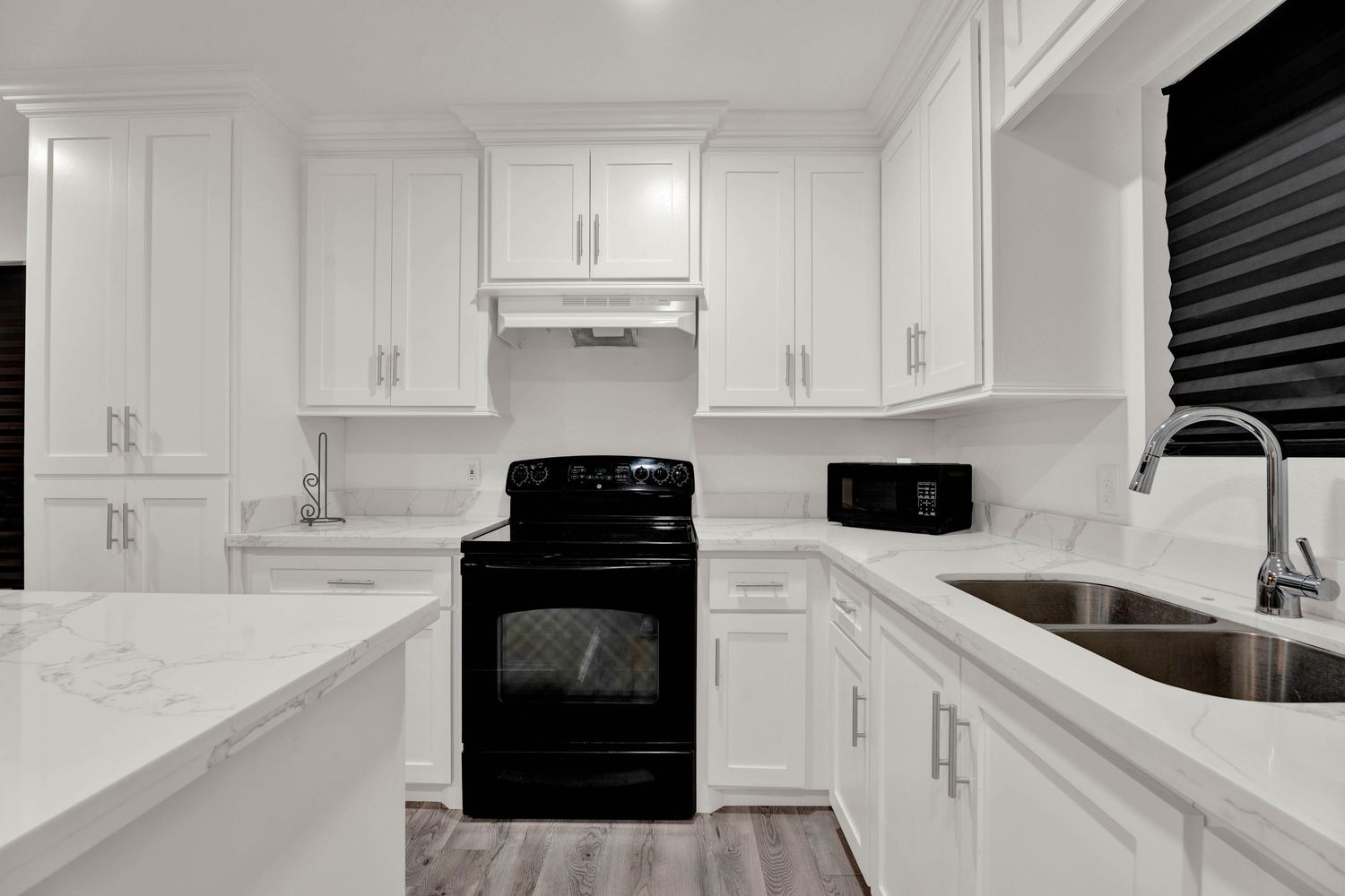White kitchen with black electric range, quartz countertops, white shaker cabinets, stainless steel sink, and hardwood floors.