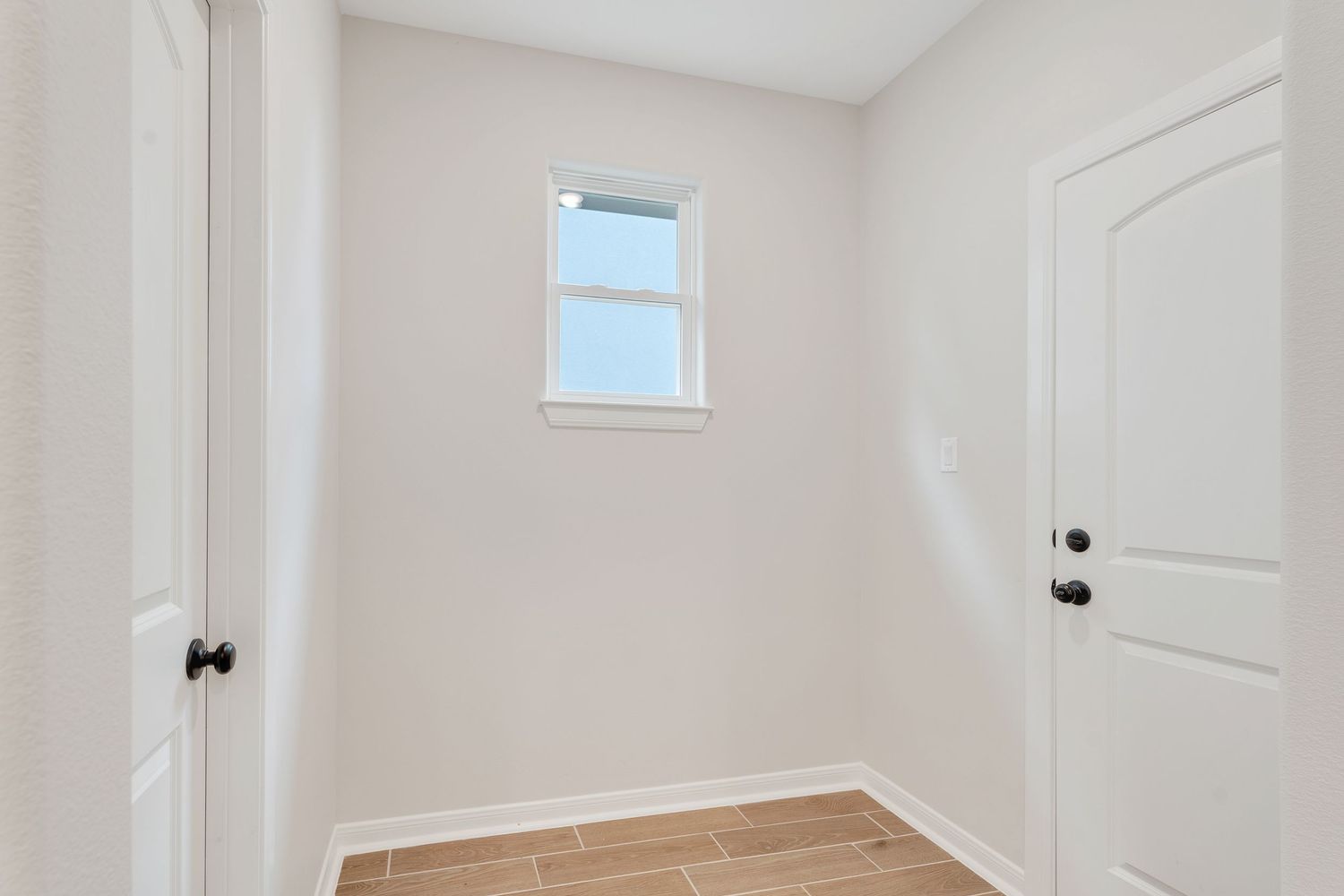White interior hallway with hardwood flooring, natural light from windows, and multiple closed doors.