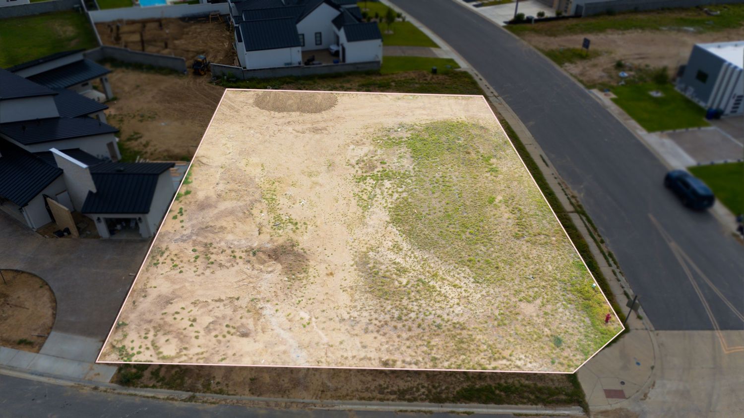 Aerial view of a cleared rectangular dirt lot bordered by a curved road and residential buildings.