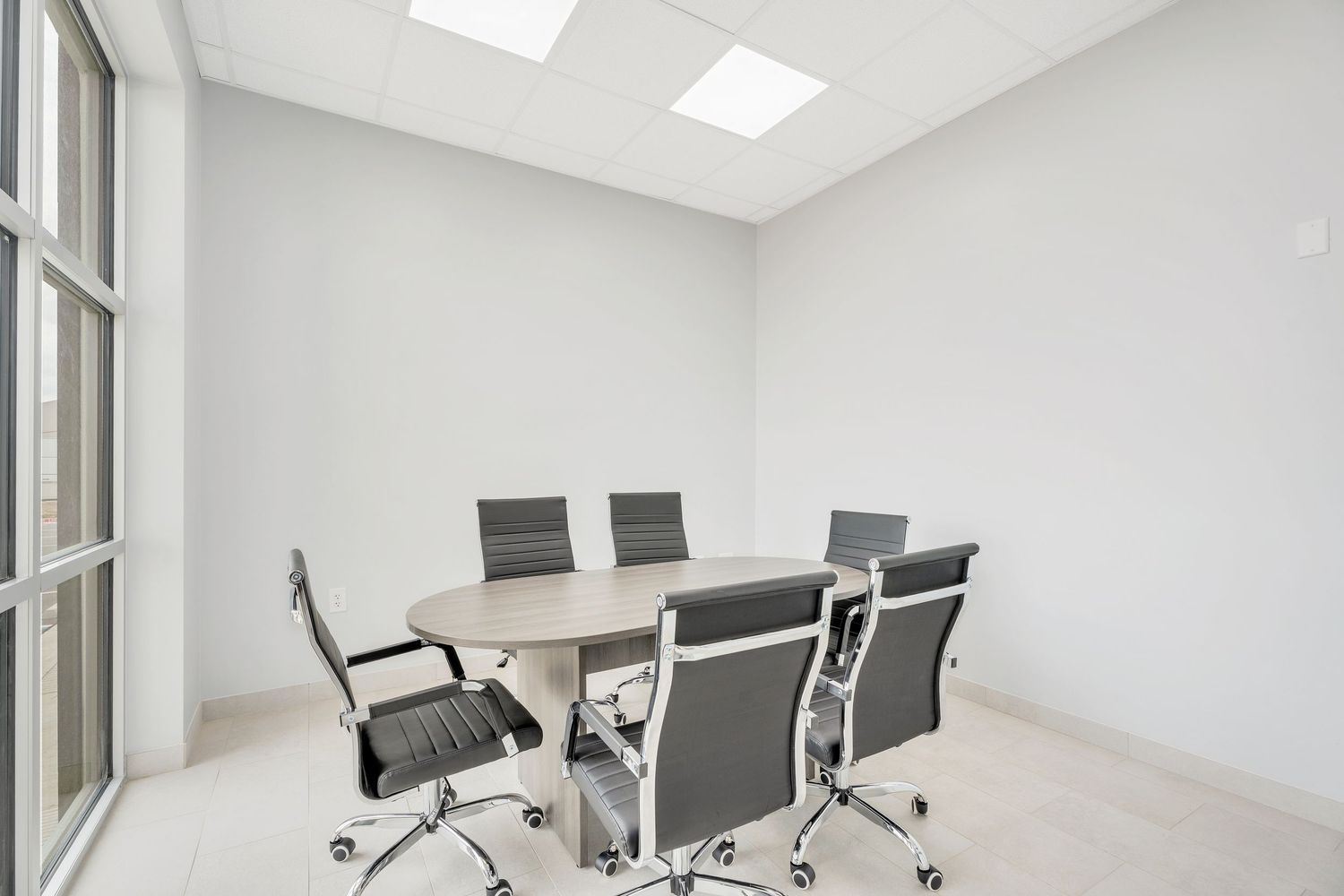 Modern conference room with white walls, glass partitions, and gray office chairs around a sleek meeting table.
