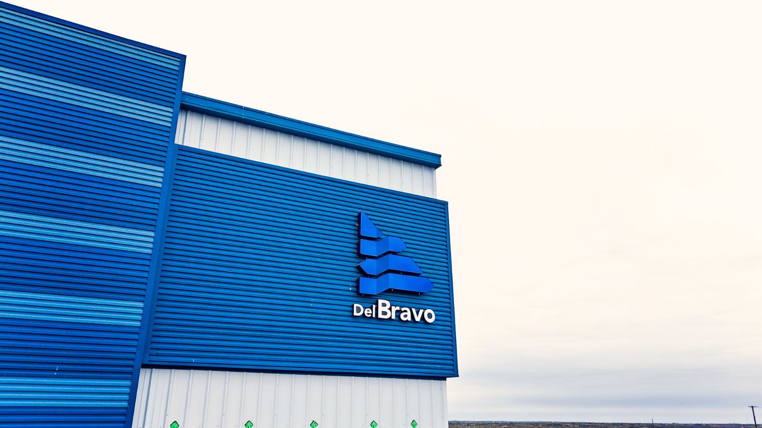 Blue and white modern industrial building exterior with DelBravo company logo on the wall.