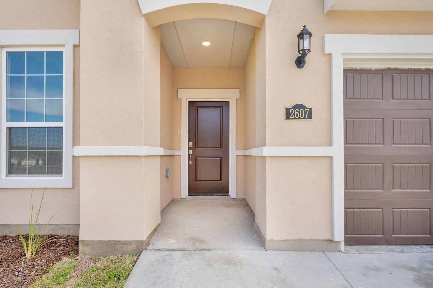 Exterior view of a modern beige stucco home with brown garage doors and architectural details.