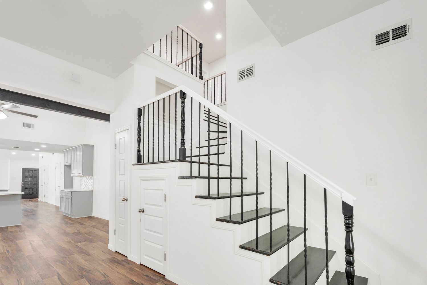 Modern white staircase with black metal railings and hardwood flooring in a bright minimalist home interior.
