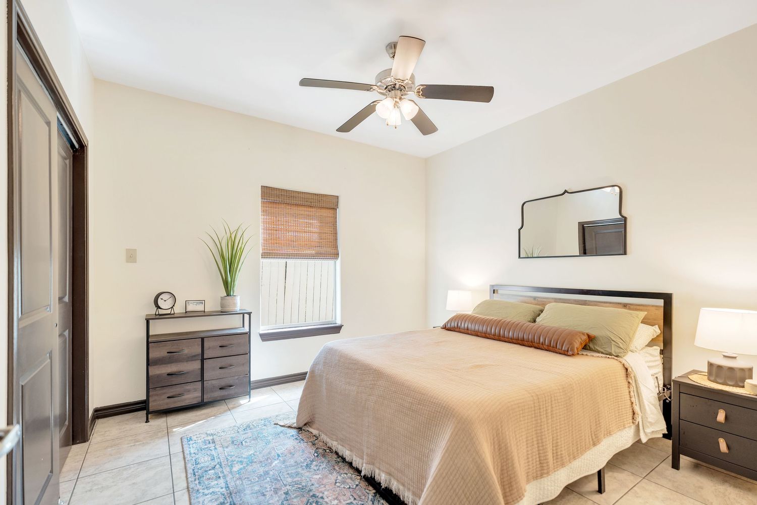 Modern bedroom with beige walls, ceiling fan, bamboo shade, gray area rug and matching furniture set.