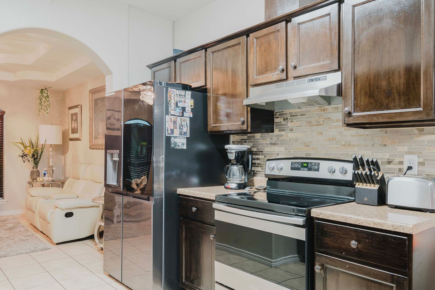 Modern kitchen interior with dark wood cabinets, stainless steel appliances, and stone backsplash extending into hallway.