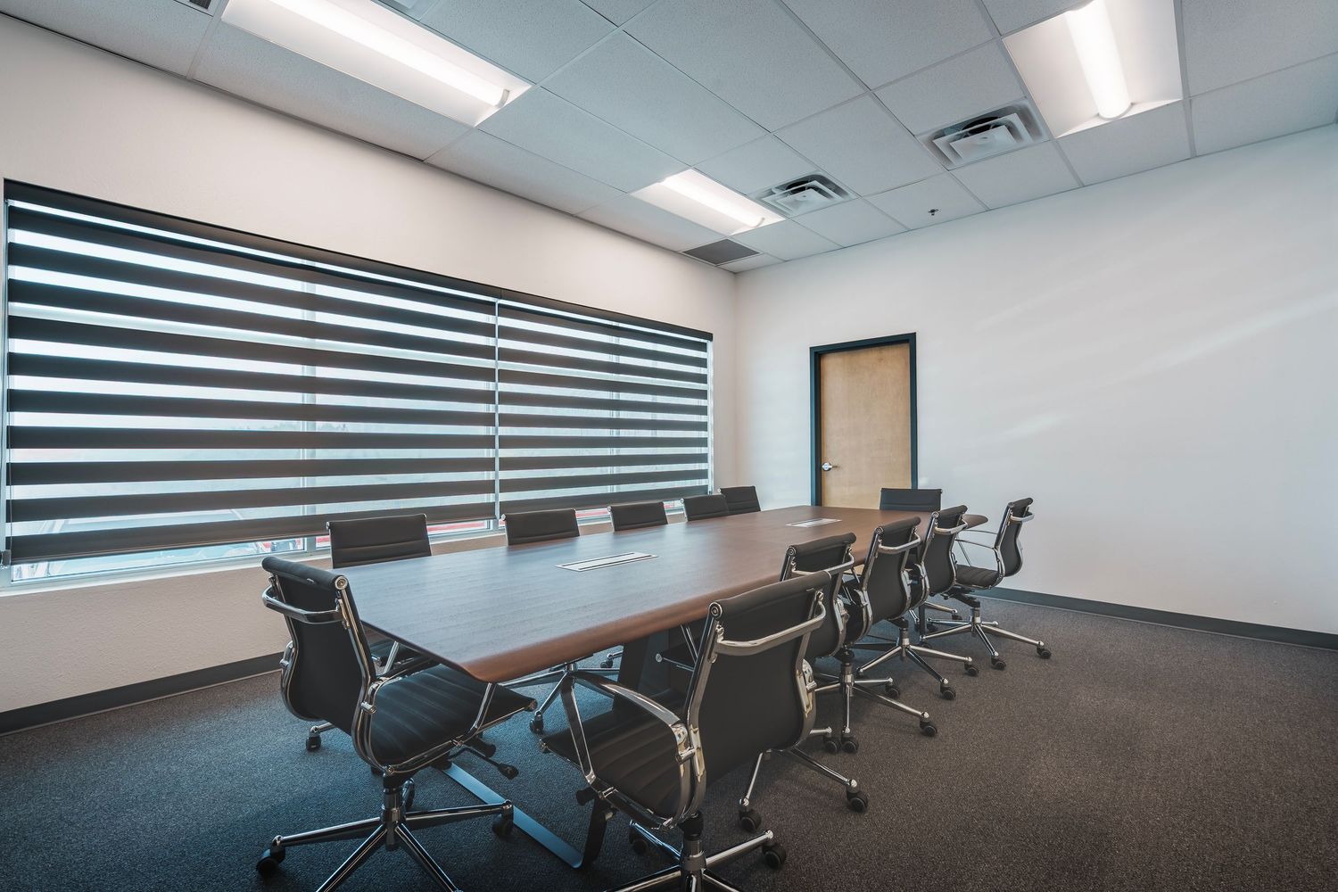 Modern conference room with sleek wooden table, black chairs and striped wall treatment in a minimalist office setting.