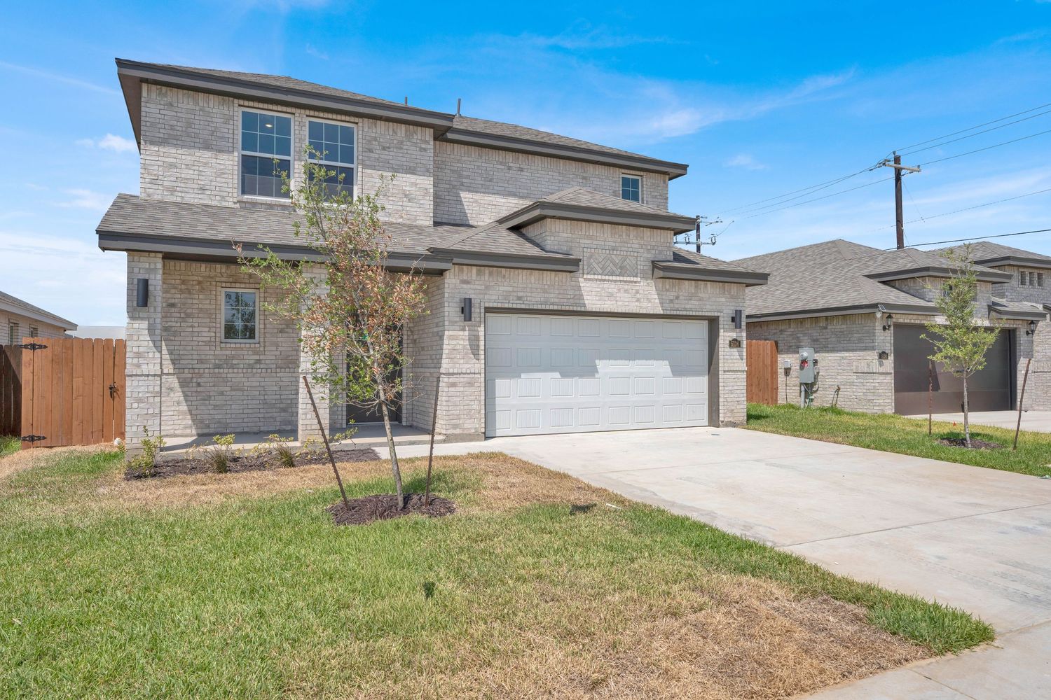 Two-story brick and stone home with two-car garage, concrete driveway, and manicured lawn under blue sky.