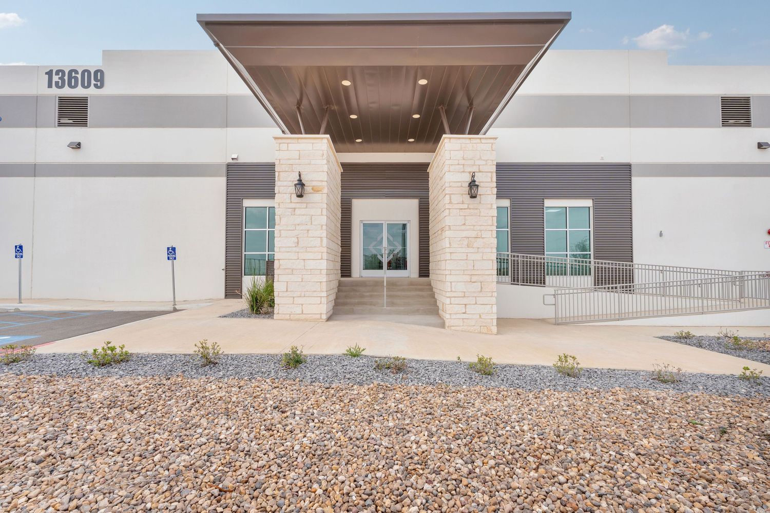 Modern commercial warehouse exterior with covered entrance and gravel landscaping under blue sky.