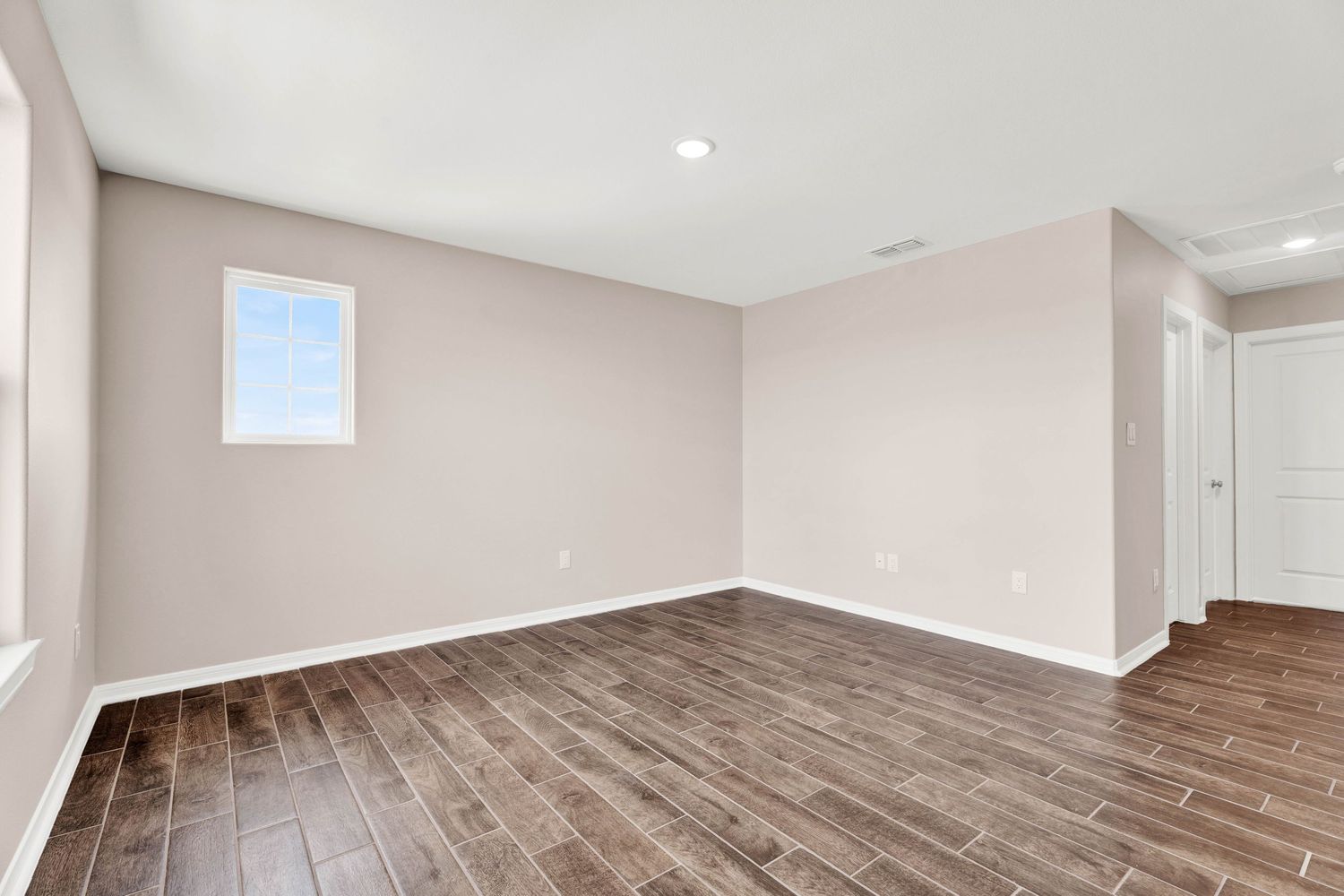 Empty room with wood-look tile floors, neutral beige walls, recessed lighting, and a small window in a modern home.