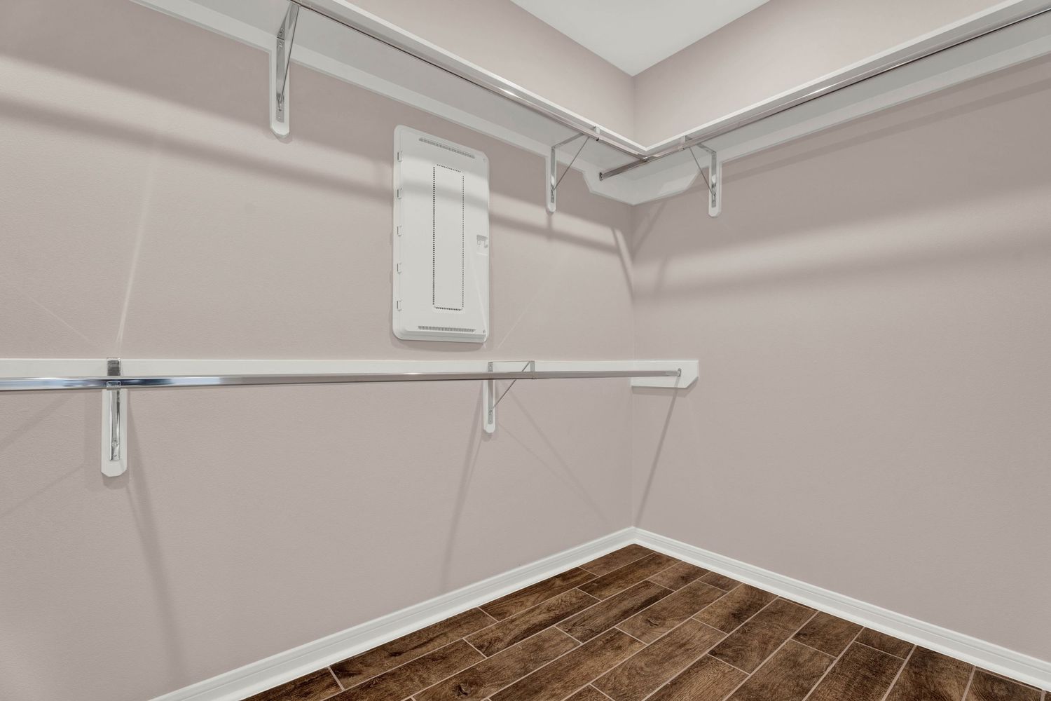 Empty walk-in closet with white double hanging rods and dark wood-look flooring in a residential home.