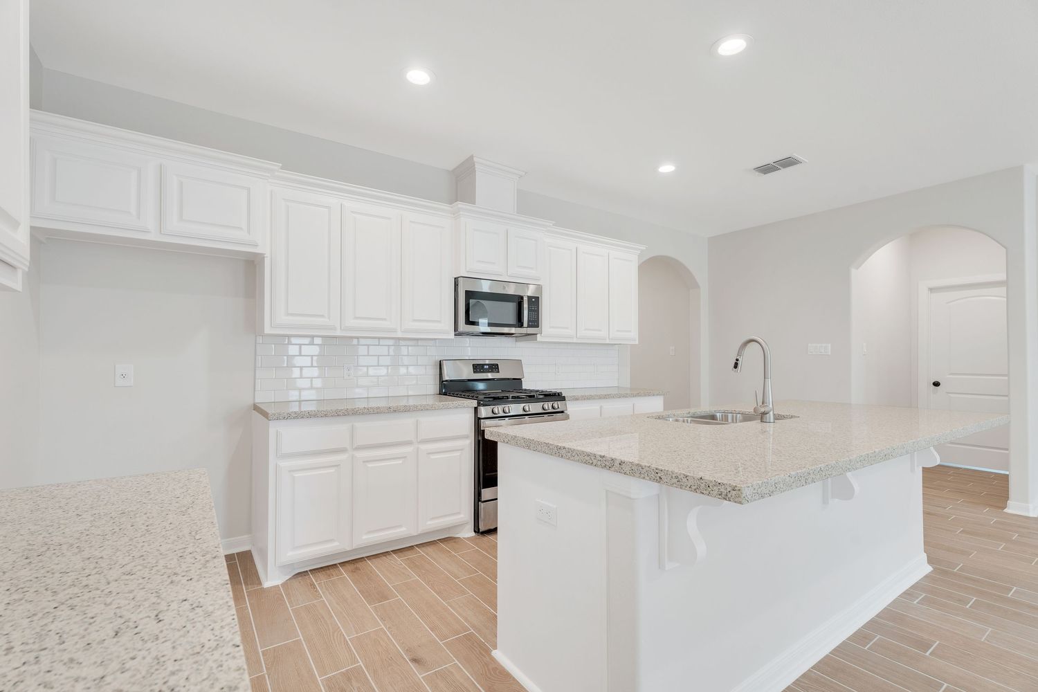 Modern white kitchen with granite countertops, stainless steel appliances, and light wood flooring features a spacious center island.