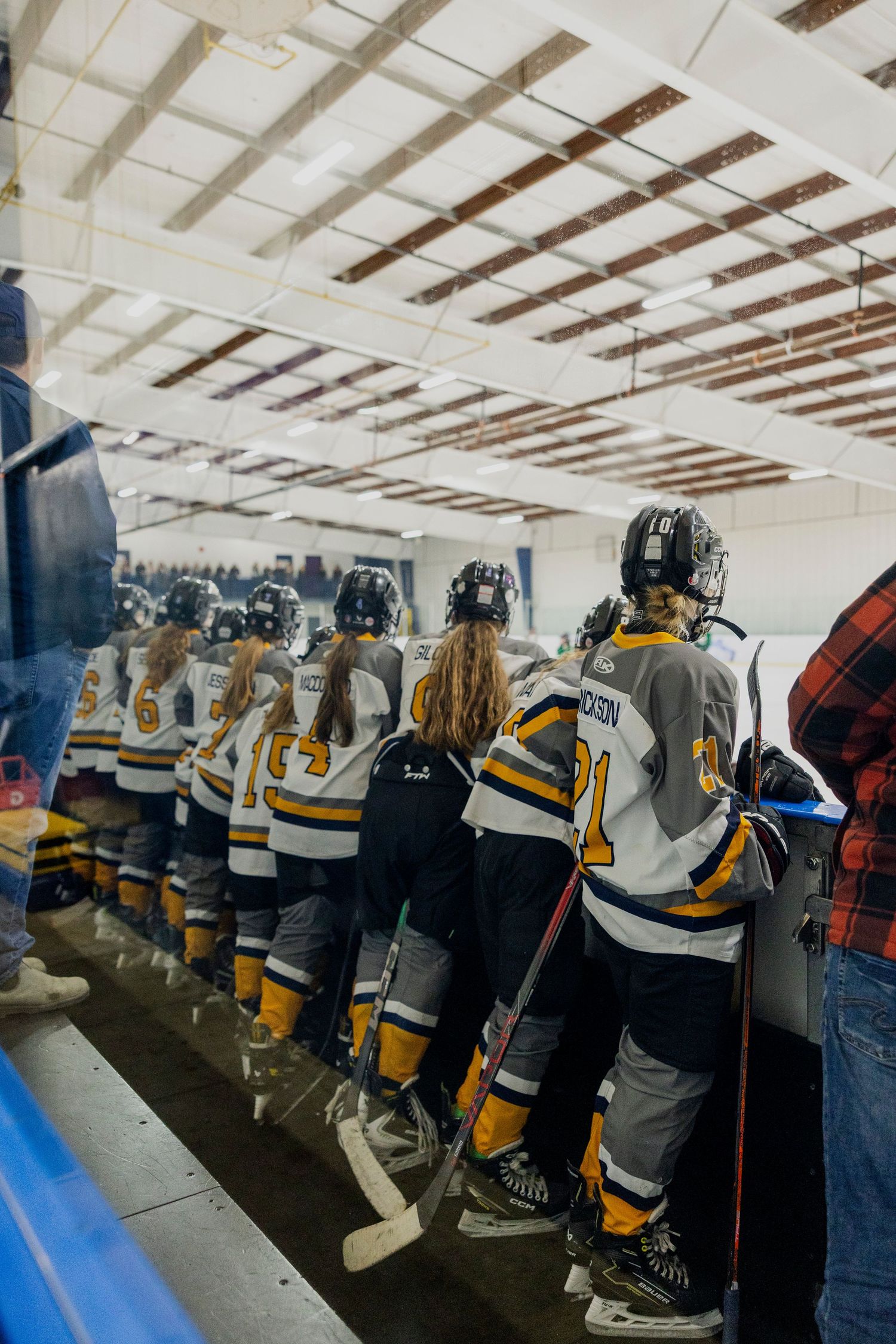 Hockey players in yellow and black jerseys line up along the boards in a locker room before a game.