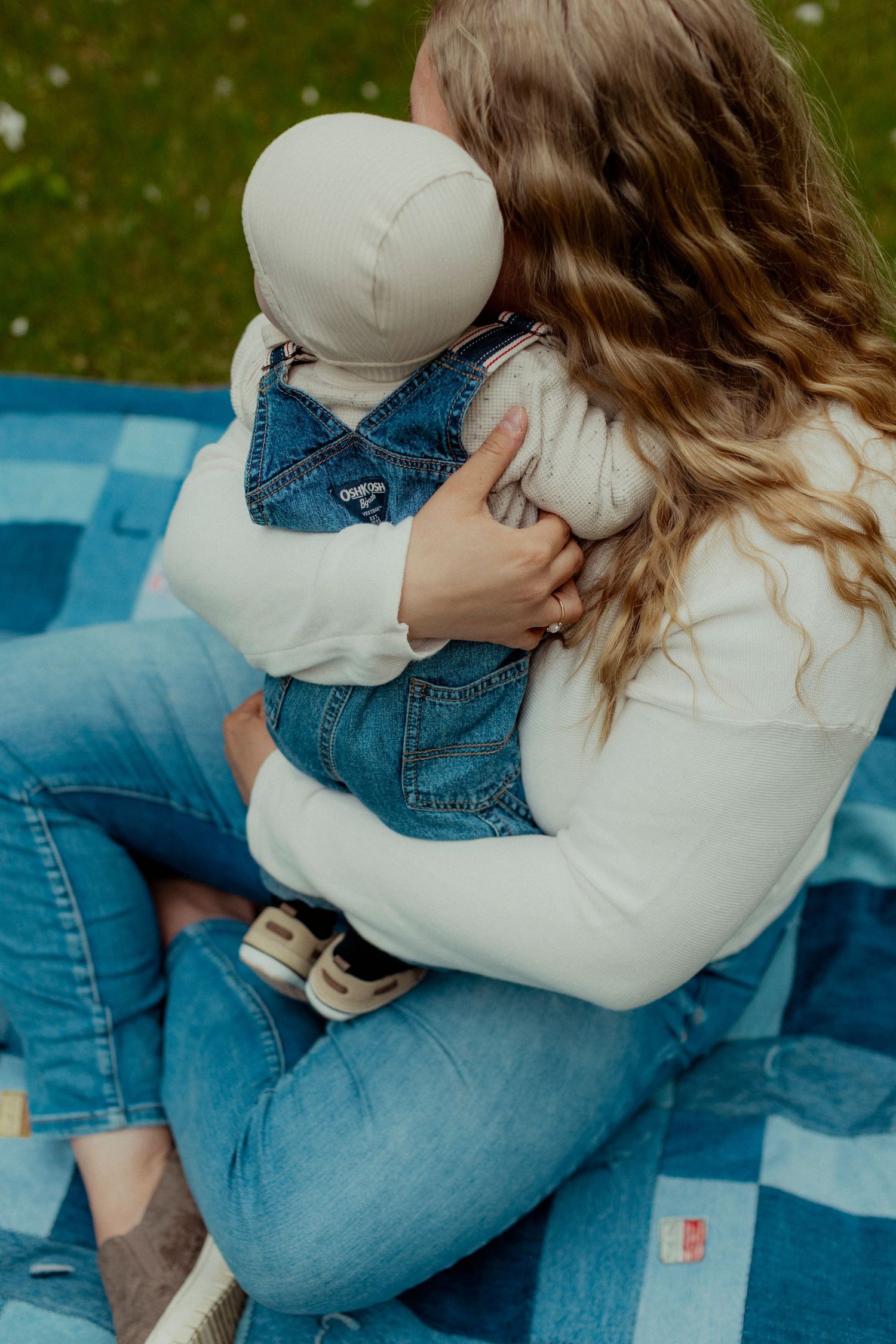A couple in denim and white clothing share an intimate embrace while sitting on blue blankets outdoors.