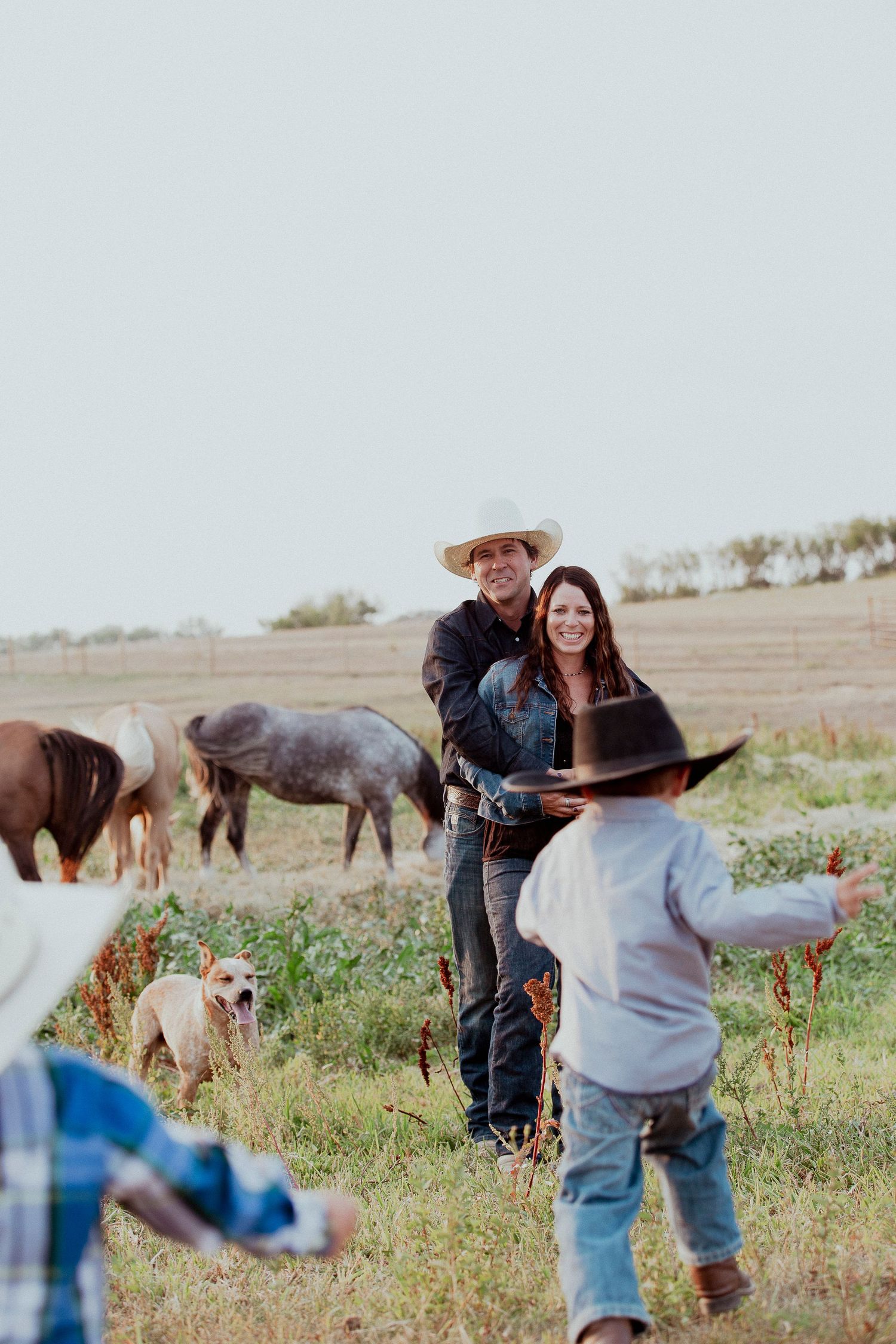 Rural family gathering outdoors with horses grazing in a rustic countryside setting, sask photographer, rural photographer, saskatchewan fam