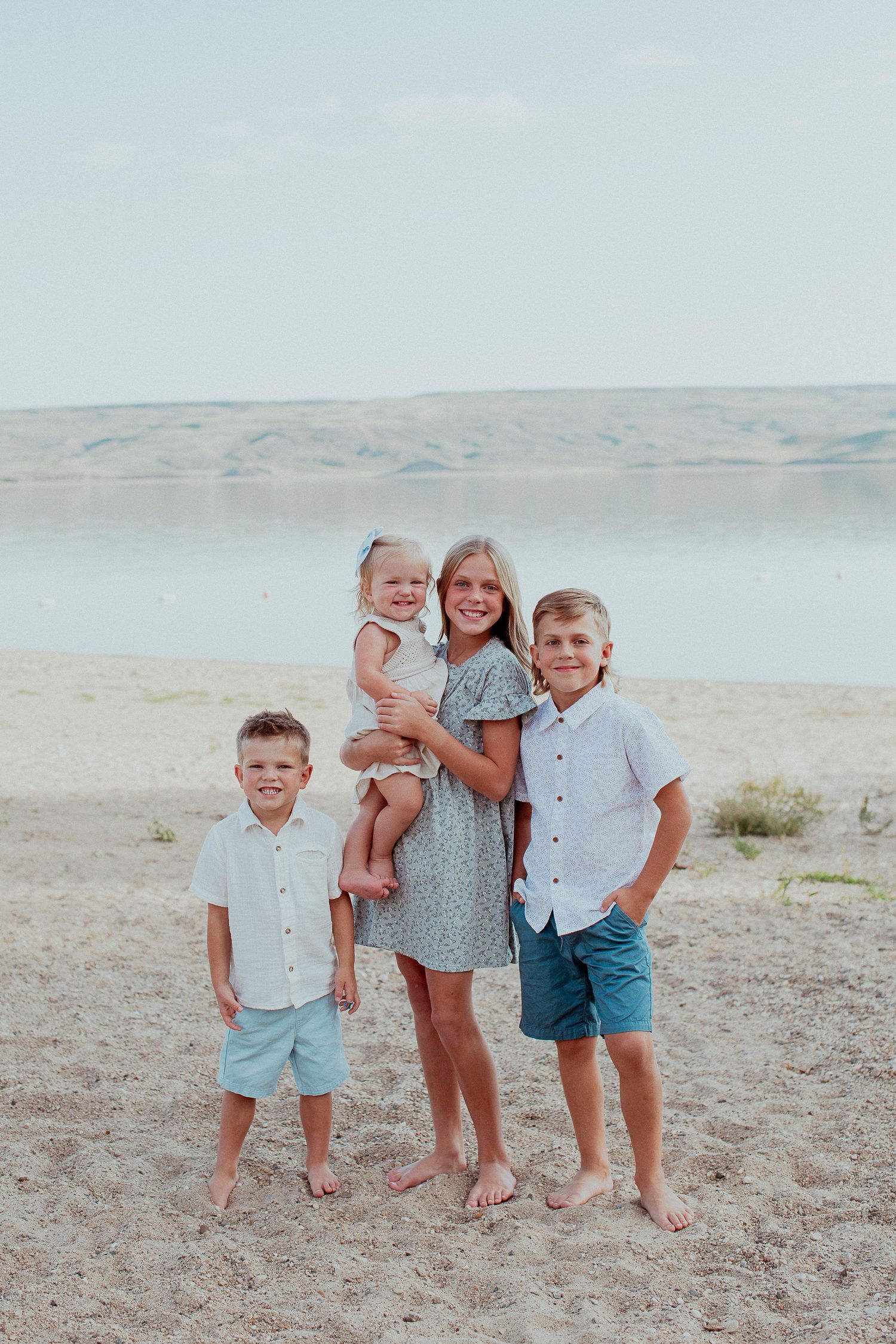Family portrait at beach with scenic desert hills and water in background.