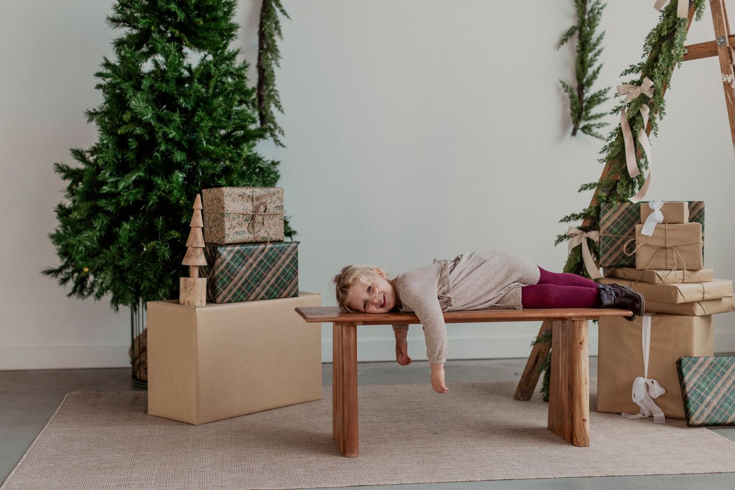 A person lies exhausted on a wooden bench surrounded by moving boxes and a small Christmas tree in the corner.