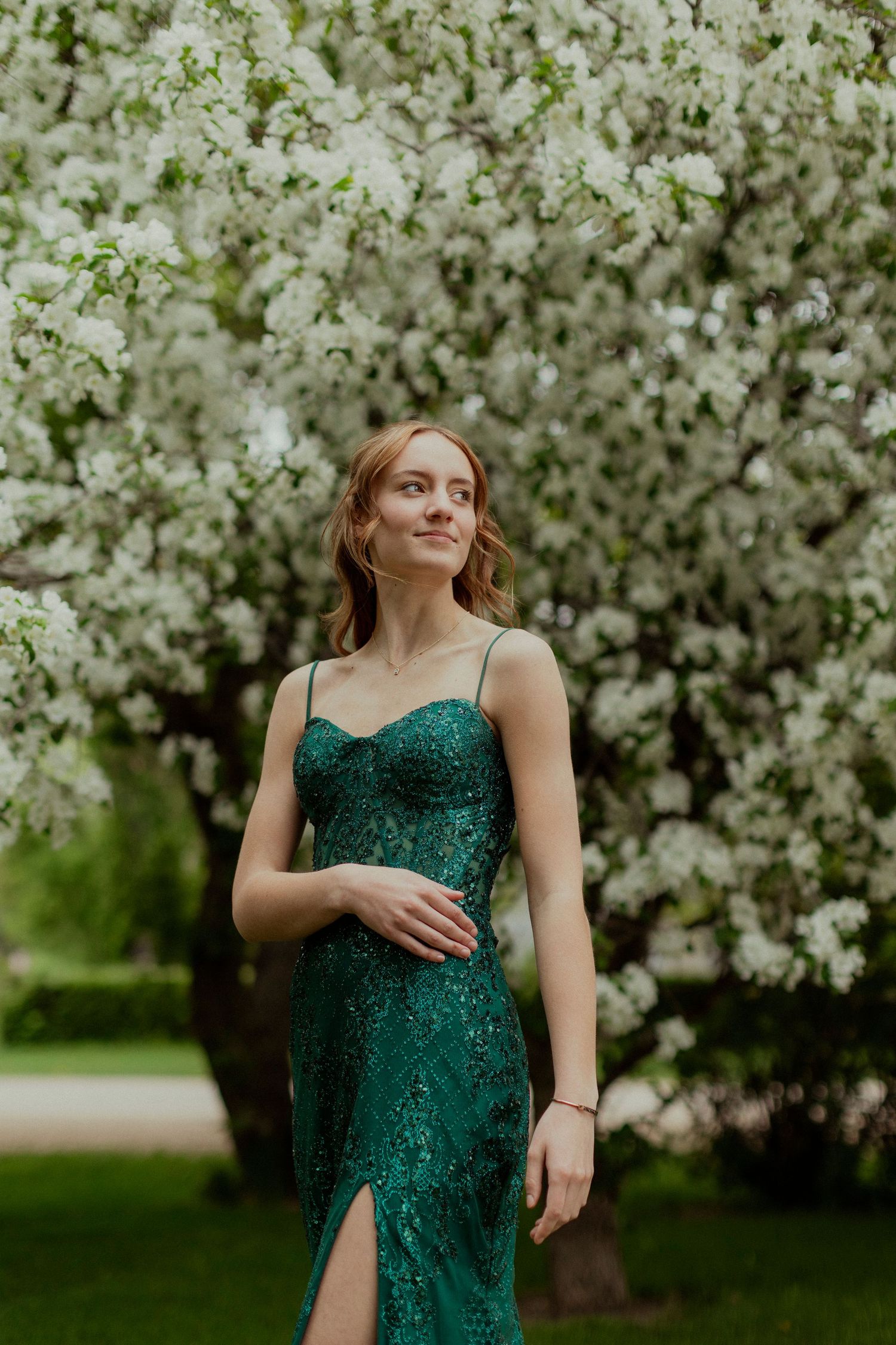 Elegant emerald green sequined dress against blooming white spring trees in a garden setting. graduate, Sask grad