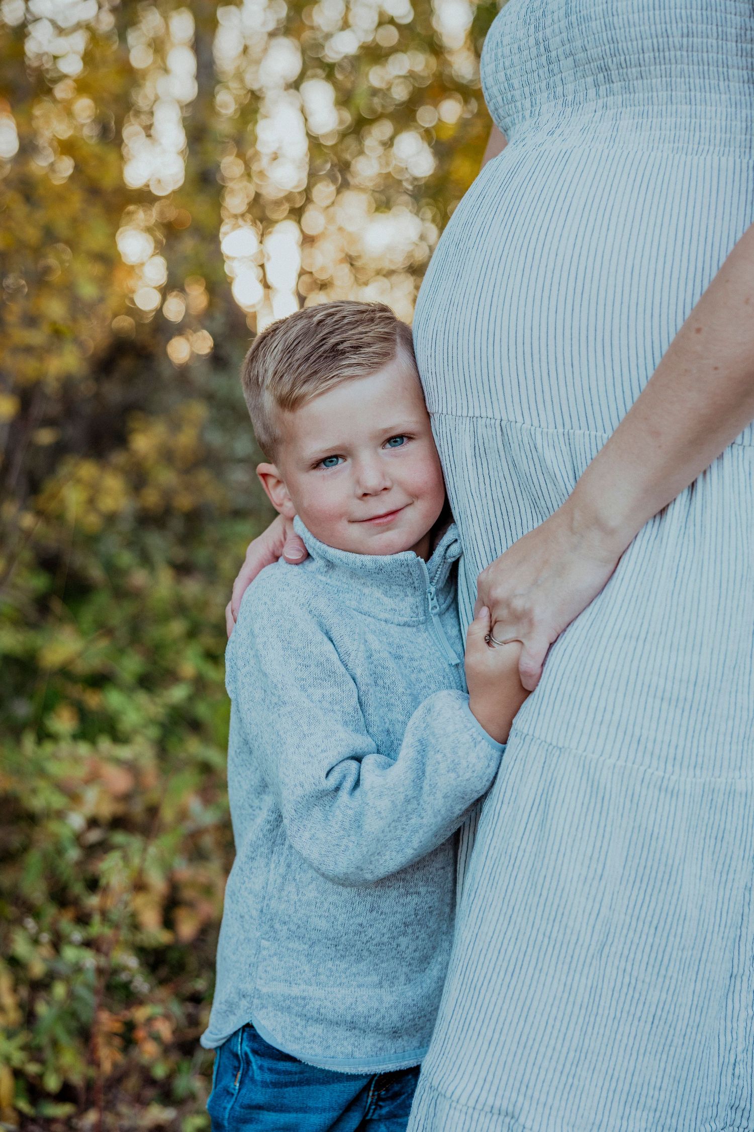 A child in a light blue sweater hugs an adult wearing matching blue in an outdoor autumn setting.