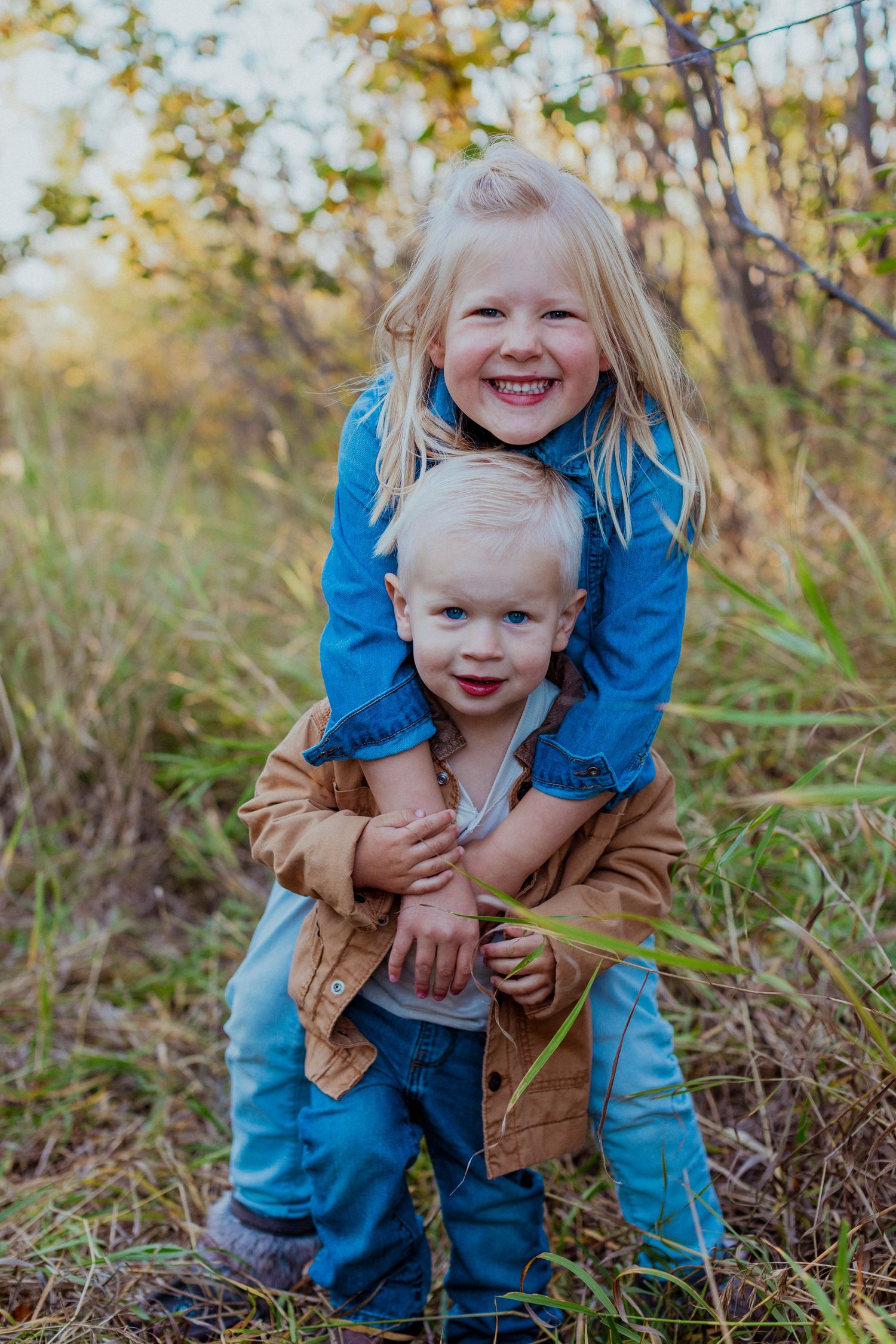 Two children playing and hugging outdoors in casual clothing during autumn.