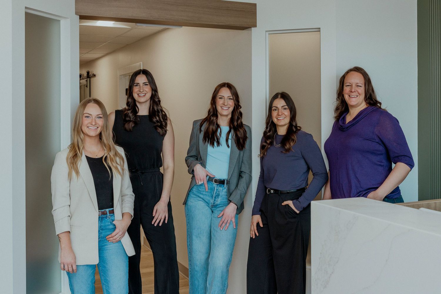 A group of healthcare workers in scrubs and professional attire stand together in a bright hallway.