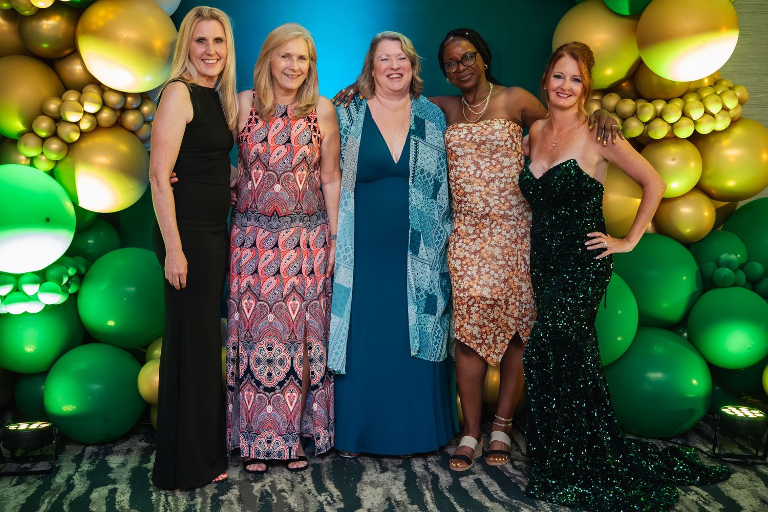 People pose together against a backdrop of green and gold balloons at a festive party celebration.