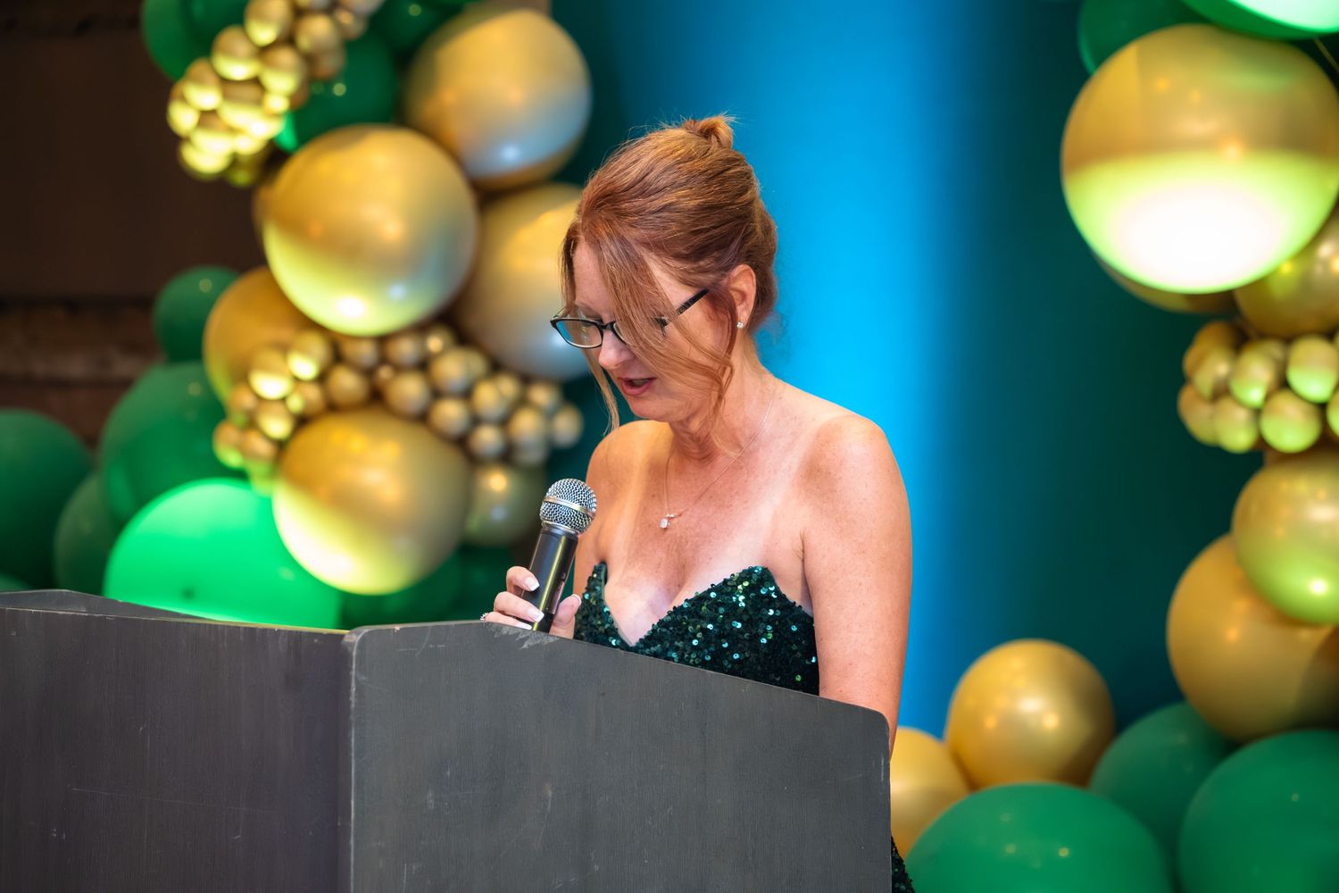 Decorative gold and green balloons create an elegant party backdrop with soft bokeh lighting effects.