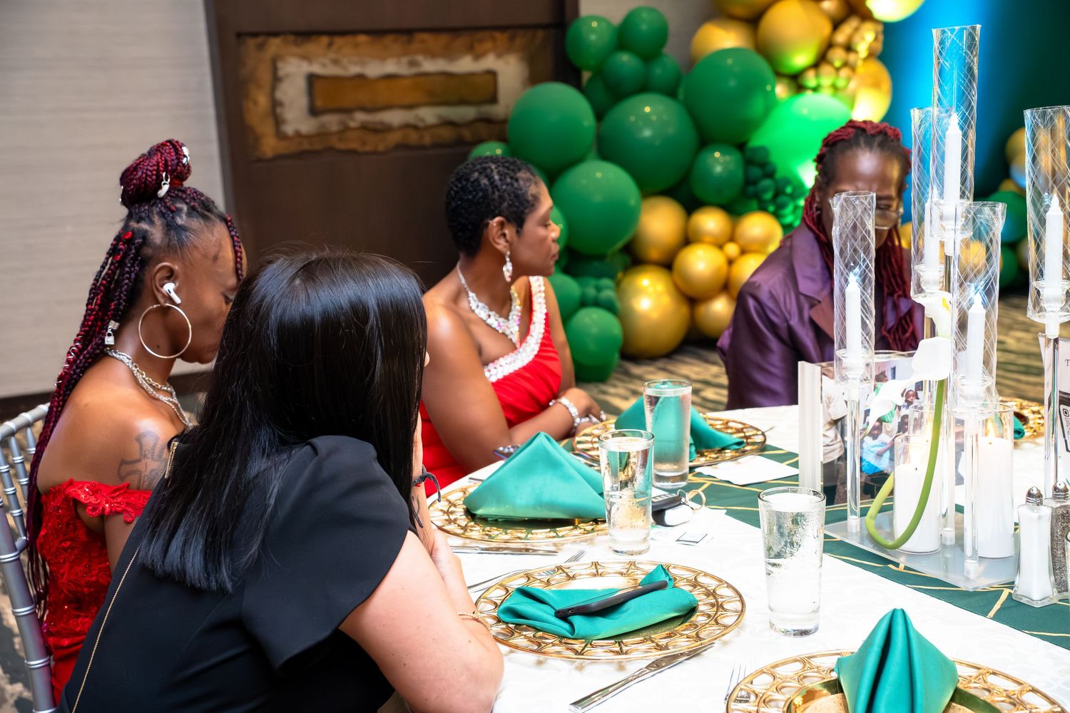 People gathered at a festive celebration with green and yellow balloon decorations at a decorated table setting.