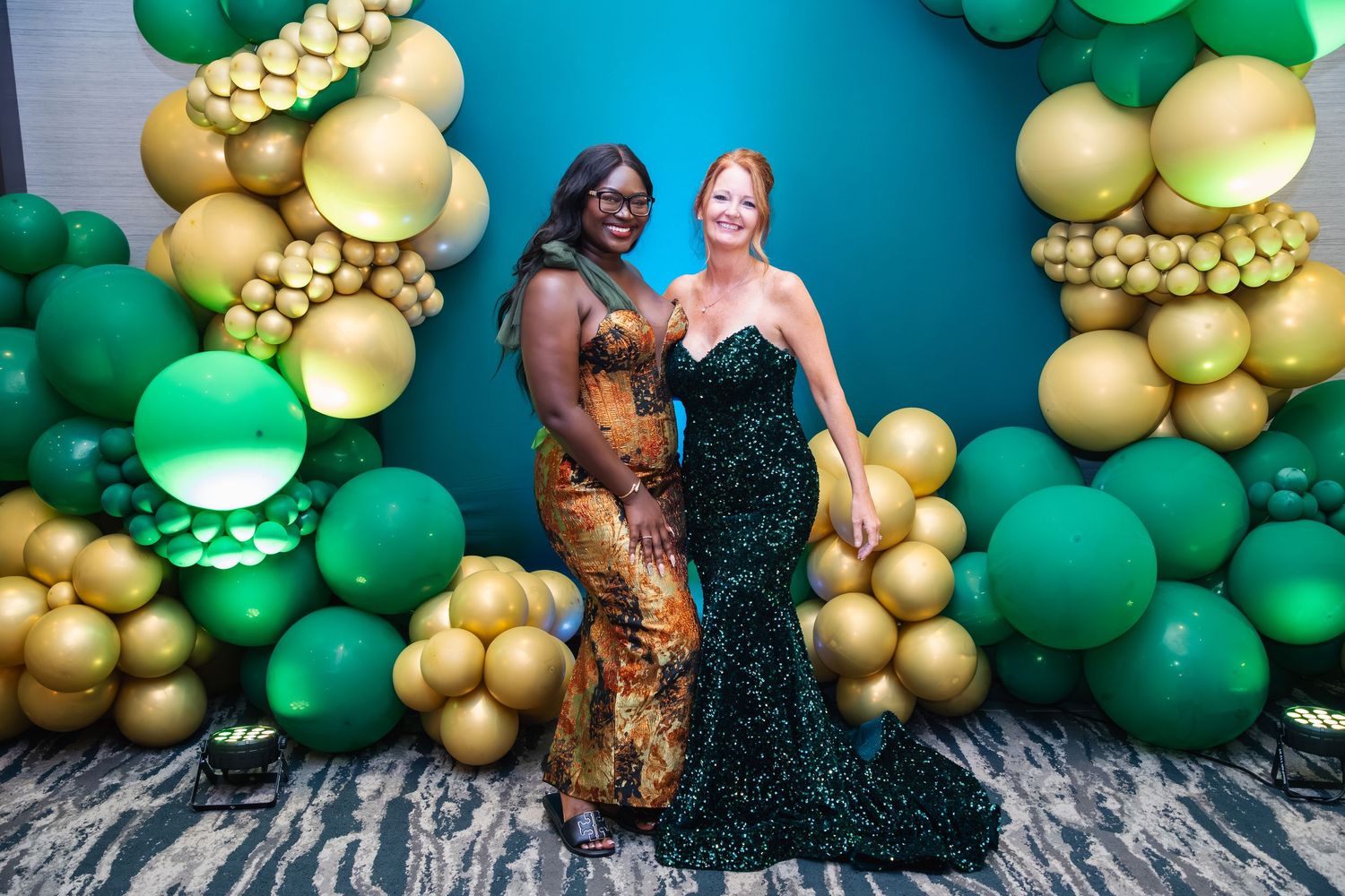 Elegant party setup with green and metallic gold balloon garland decorations against a teal backdrop.