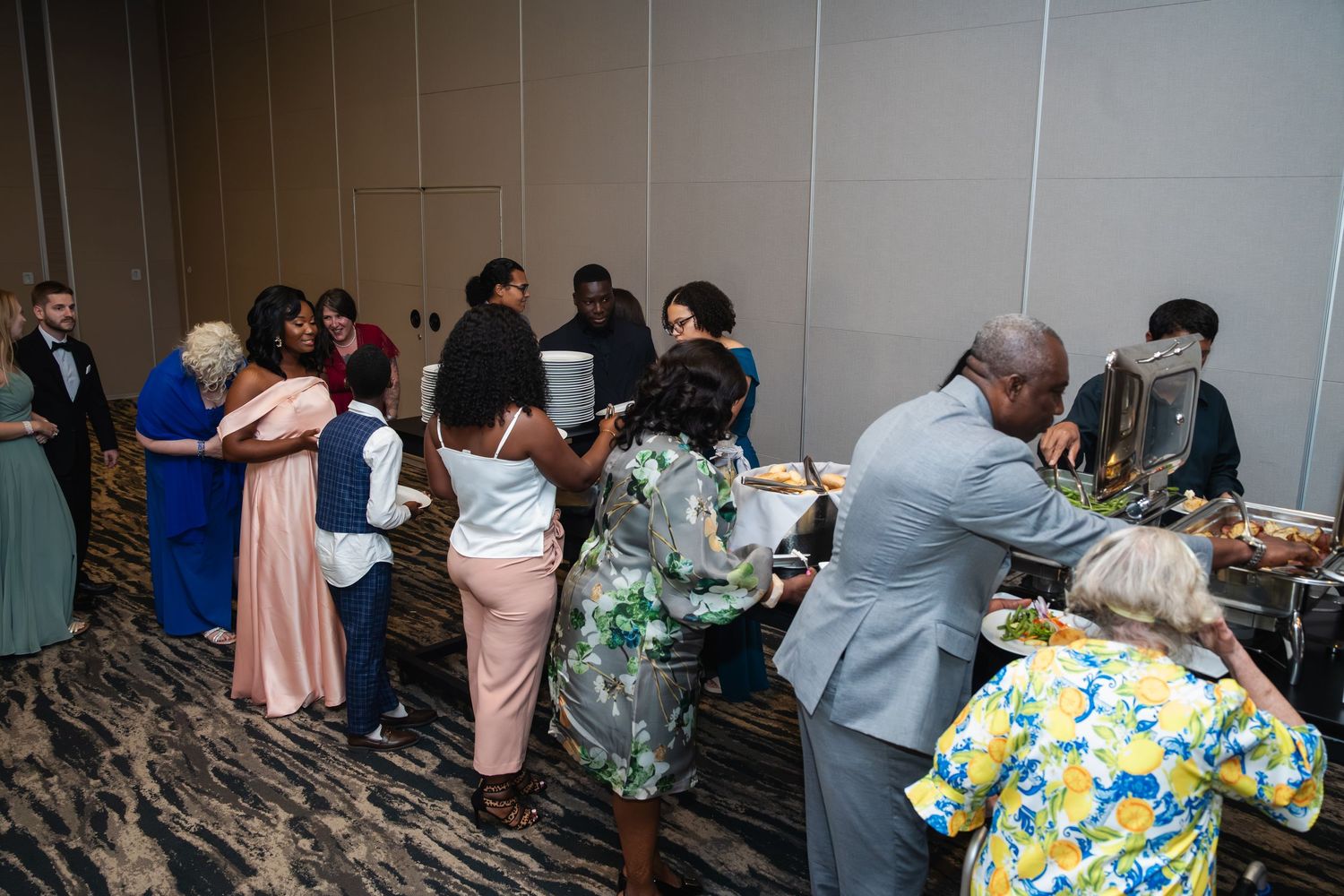 A group gathers in a formal event space with pink and gray decor visible in the background.