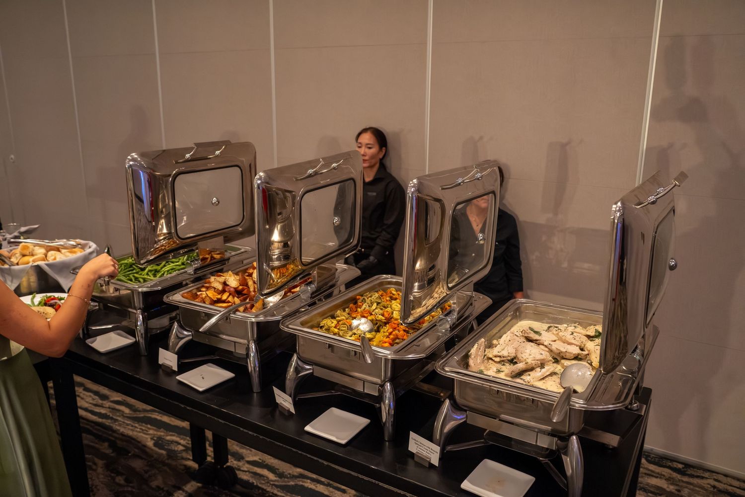 A buffet line with chafing dishes and serving stations displaying various food items in a catering setup.