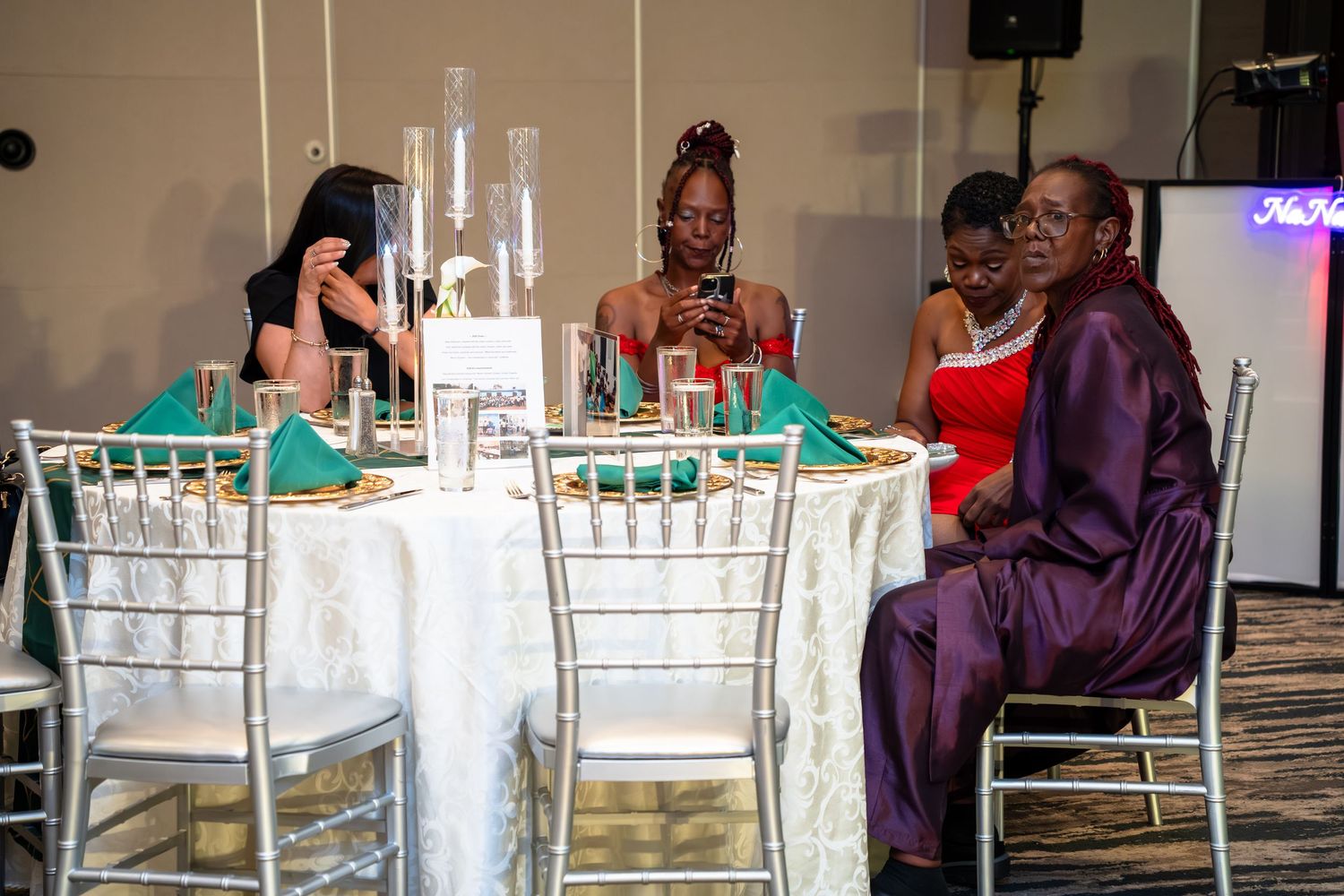 Guests enjoy conversation and drinks at an elegant table with silver Chiavari chairs and turquoise accents at a formal event.