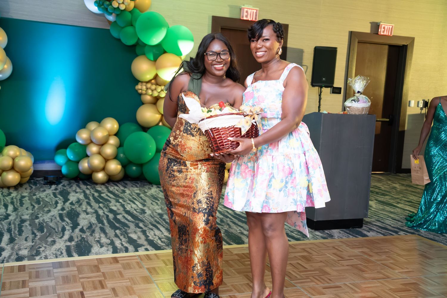 Festive party room decorated with green and gold balloons featuring guests celebrating in formal attire.