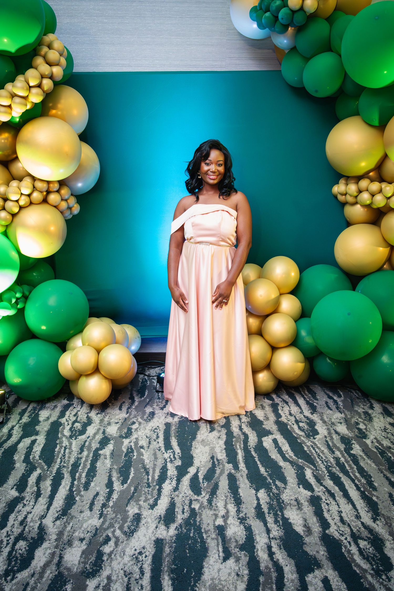 Festive balloon arch display featuring green and gold balloons against a blue wall with textured base decoration.