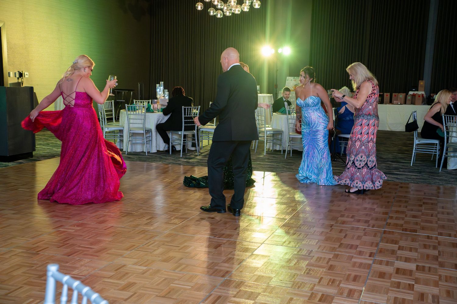 Couples in formal attire dance together on a wooden ballroom floor during an elegant evening event.