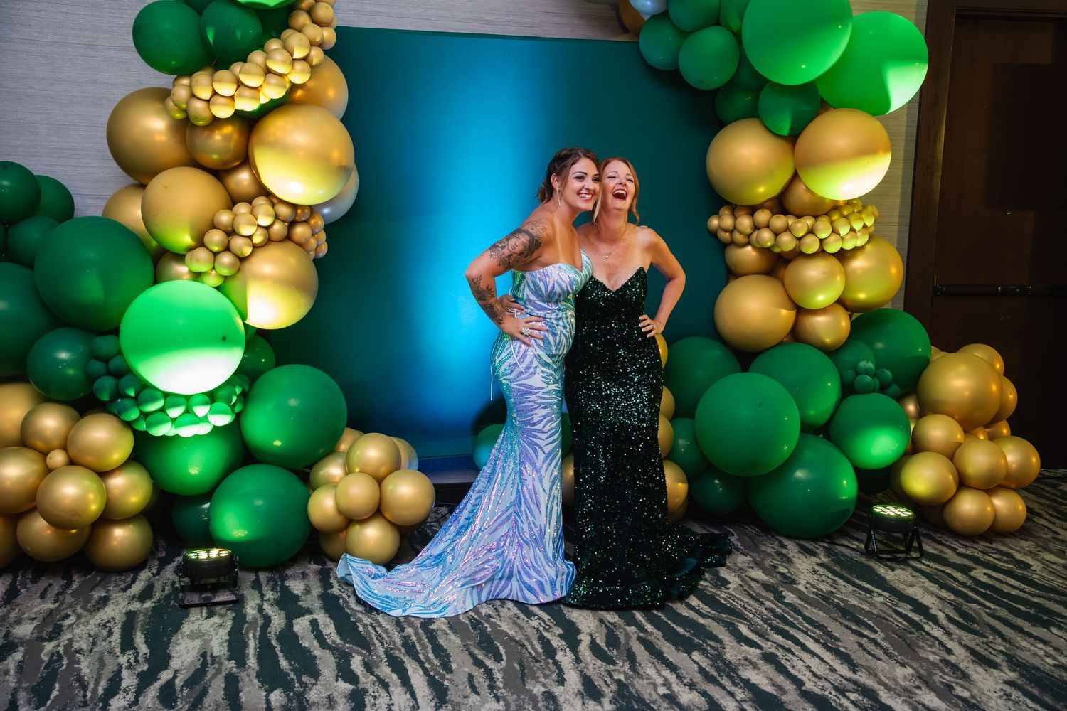 Elegant formal event setup with green and gold balloon arch decorations against a teal backdrop.