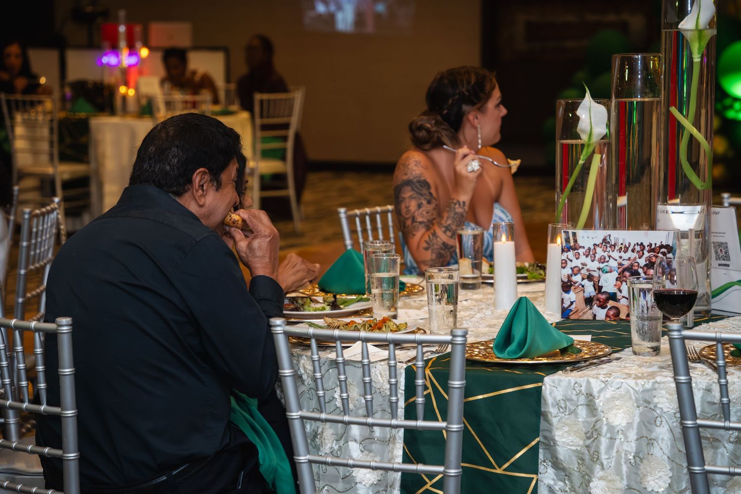 Wedding guests sit at elegantly decorated reception tables with white linens and floral centerpieces.