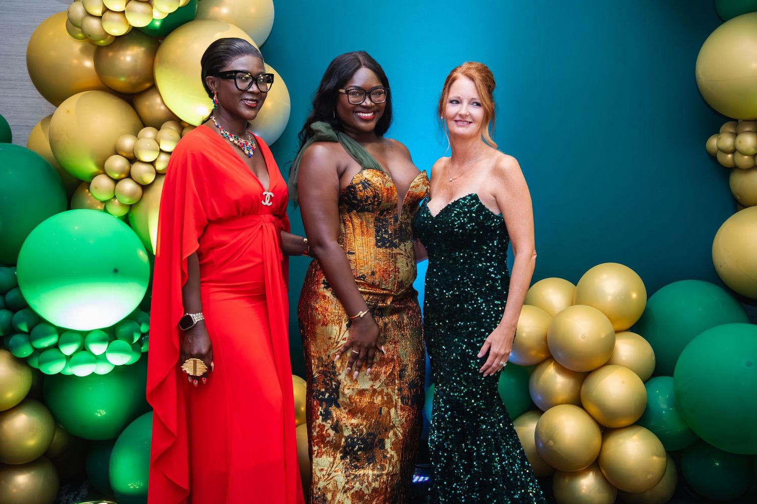 Festive party scene with gold balloon decorations and people gathered against a teal backdrop at an elegant event.