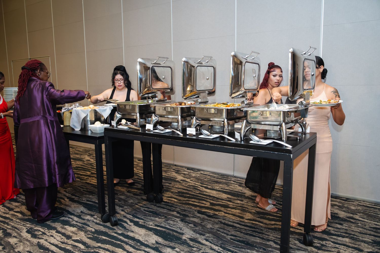 A row of people standing at registration tables in a hotel conference area with patterned carpet and beige walls.