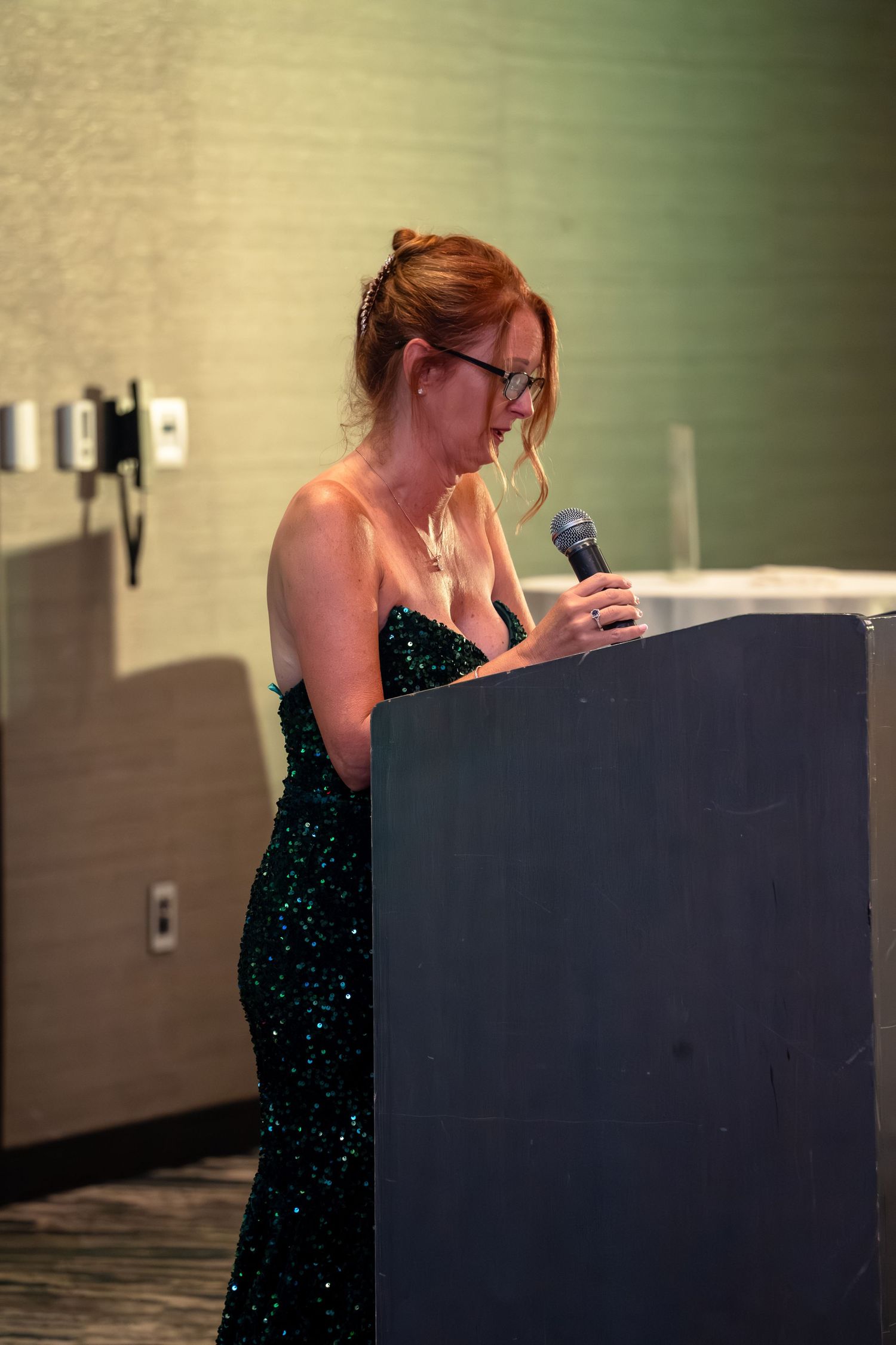 A performer in a sparkly black dress shows emotion while standing at a podium during a presentation.
