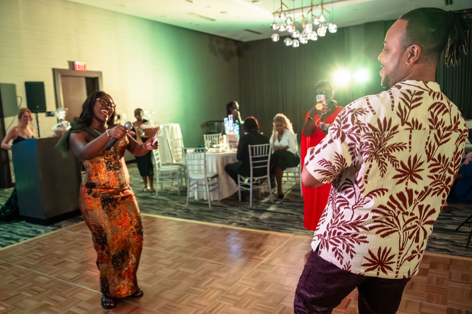People dancing together at a social event in a room with green walls and ambient lighting.