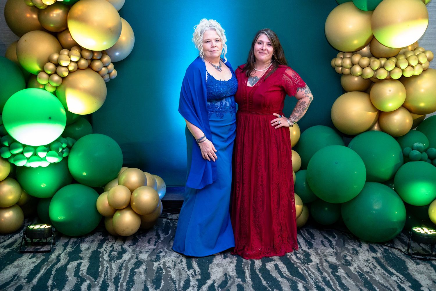 Festive balloon wall display featuring green and gold balloons arranged in elegant patterns against a blue backdrop.