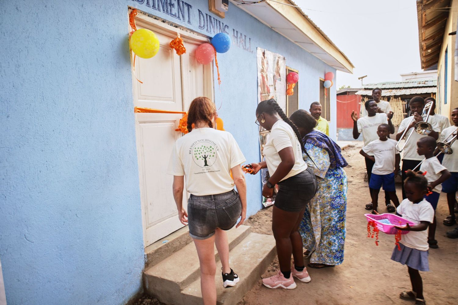 People gathering outside a blue building with festive decorations and balloons.