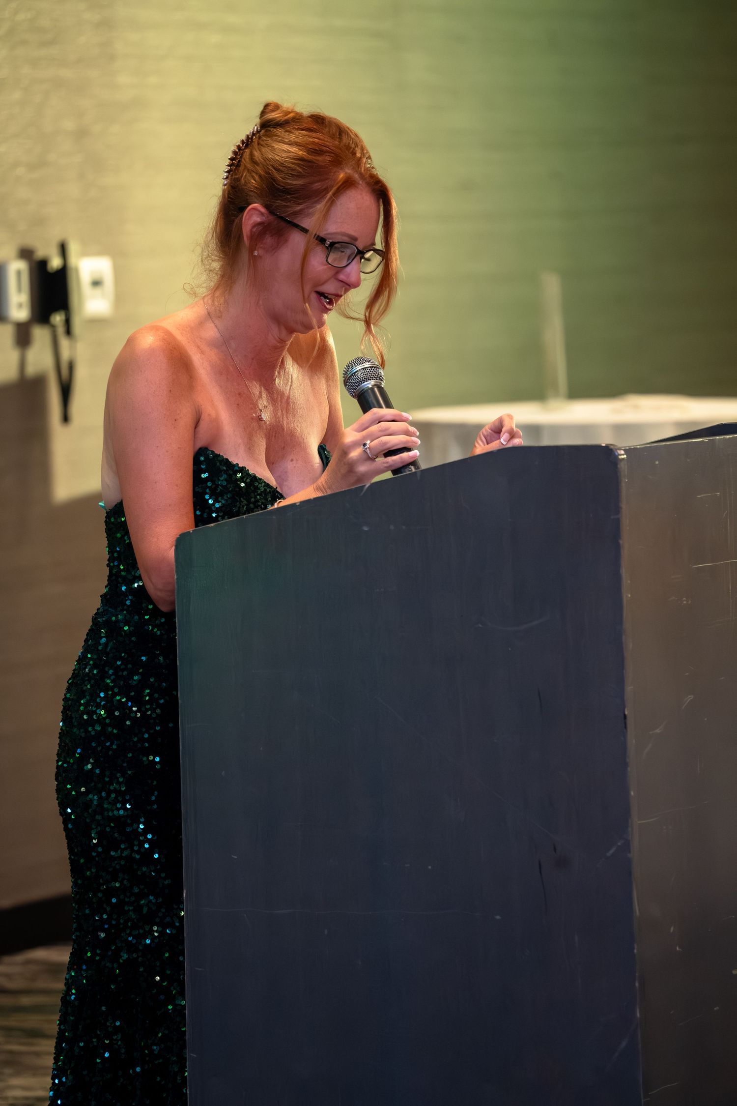 A performer in a sparkly black dress stands at a podium during what appears to be a speaking engagement.