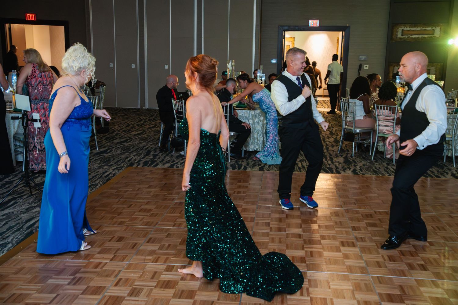 People dancing and socializing at a formal event on a parquet dance floor with guests in elegant evening attire.